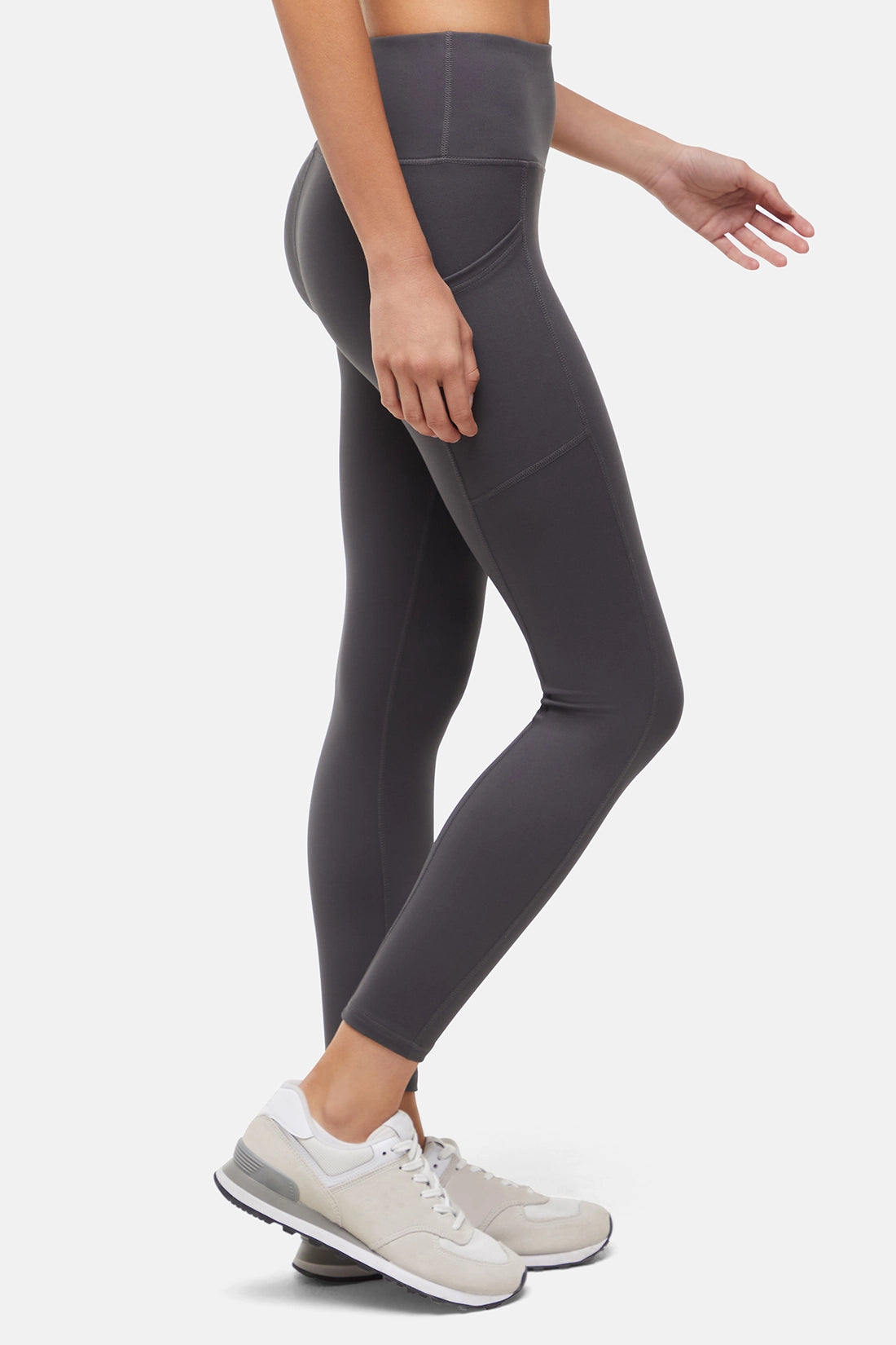Side view of woman wearing dark gray leggings with a white background.