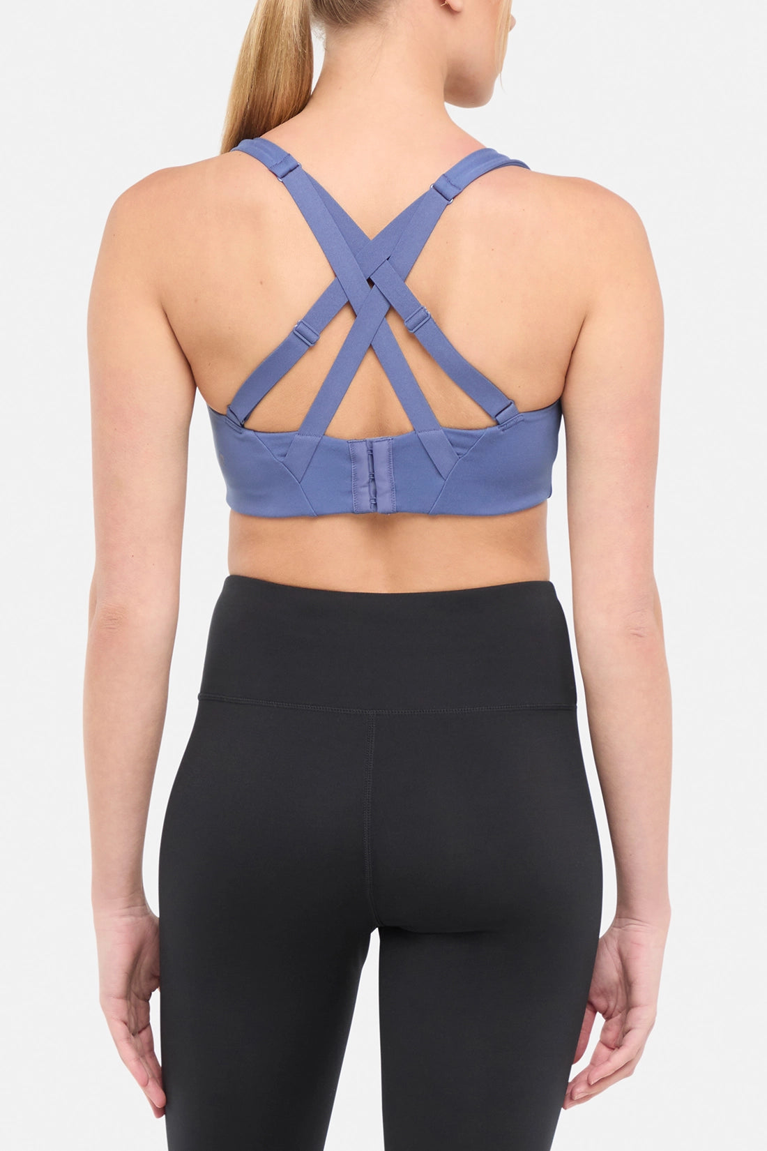 Back view of blue sports bra with strappy crisscross straps on a plain background.