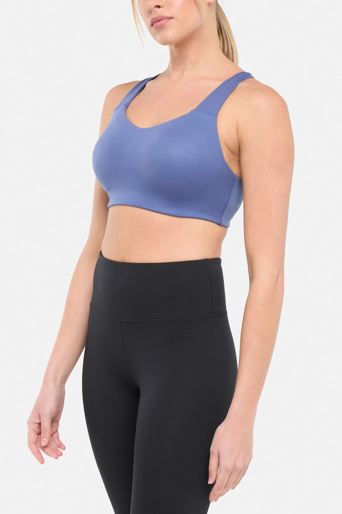 Side view of woman wearing a blue sports bra and black leggings on a white background.