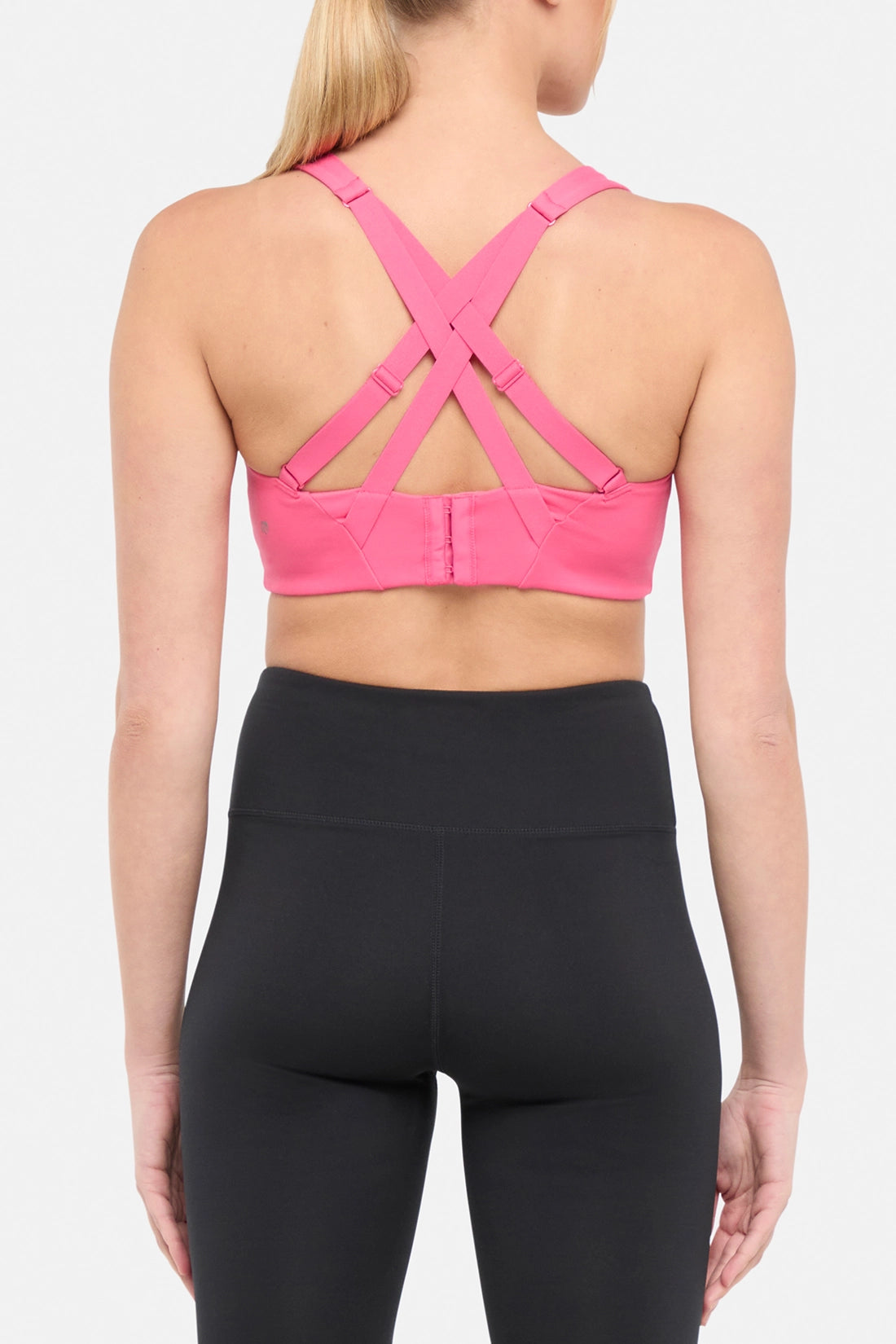 Back view of pink sports bra with strappy crisscross straps on a plain background.