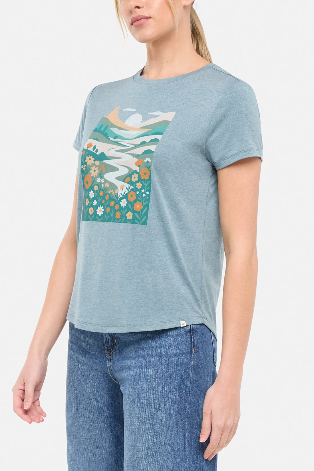 Side view of woman wearing a blue t-shirt with nature-themed graphic design on a white background.