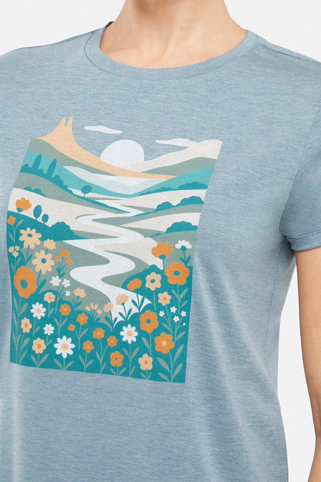 Close up view of woman wearing a blue t-shirt with nature-themed graphic design on a white background.