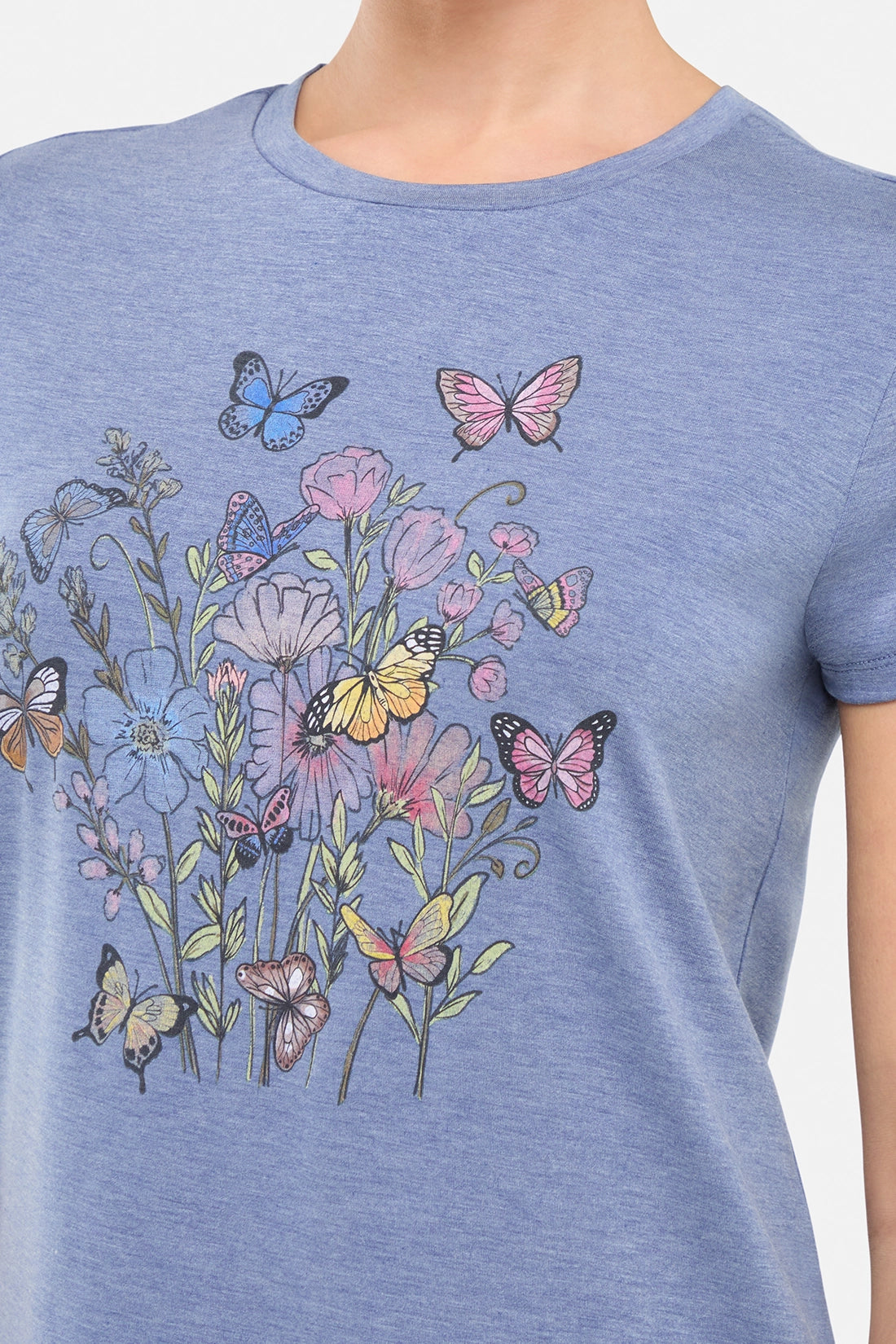 Close up view of woman wearing a blue t-shirt with butterflies and floral design on a white background.