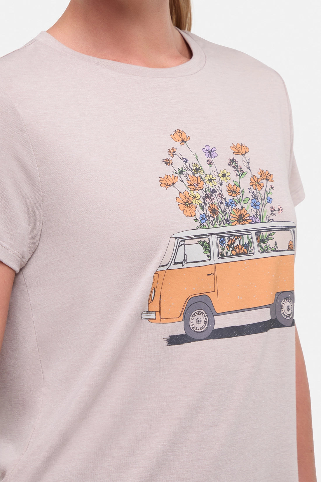 Close up front view of woman wearing a beige t-shirt with a graphic of an orange van and flowers on a .white background.