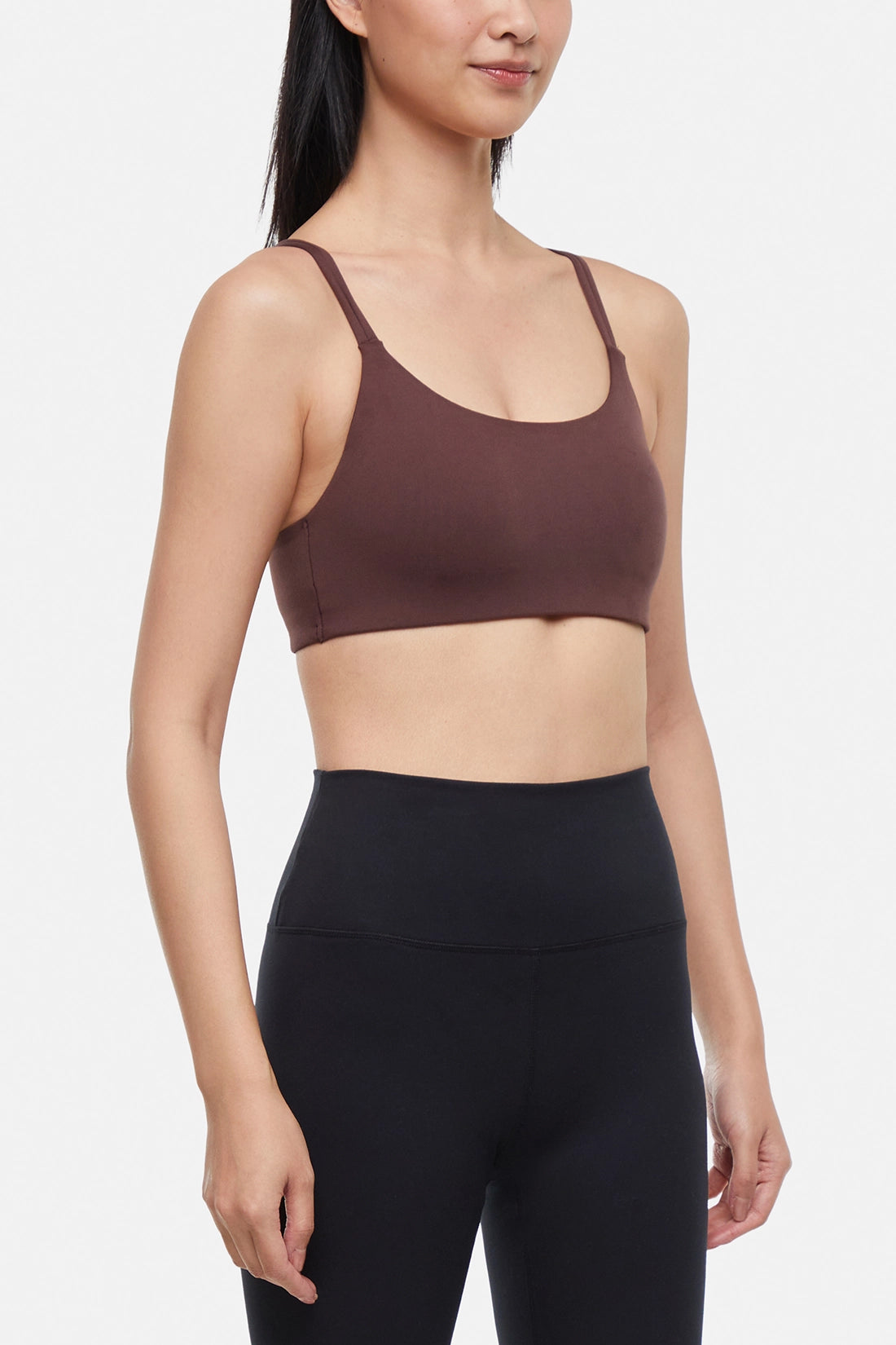 Front view of woman wearing a brown sports bra and black leggings on a white background.