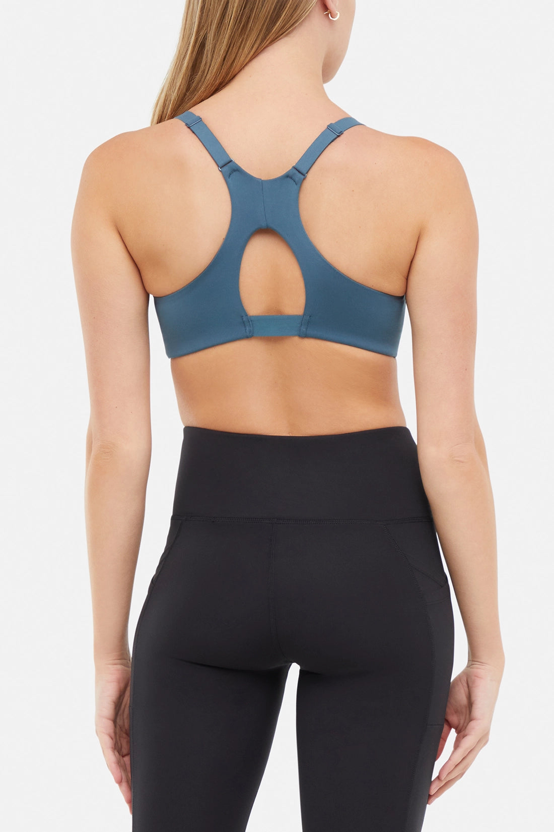 Back view of woman wearing a blue sports bra and leggings on a white background.