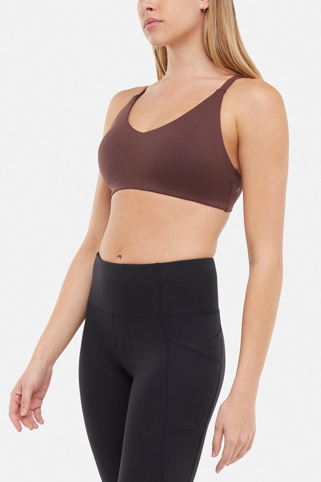 Side front view of woman wearing a brown sports bra and black leggings on a white background.
