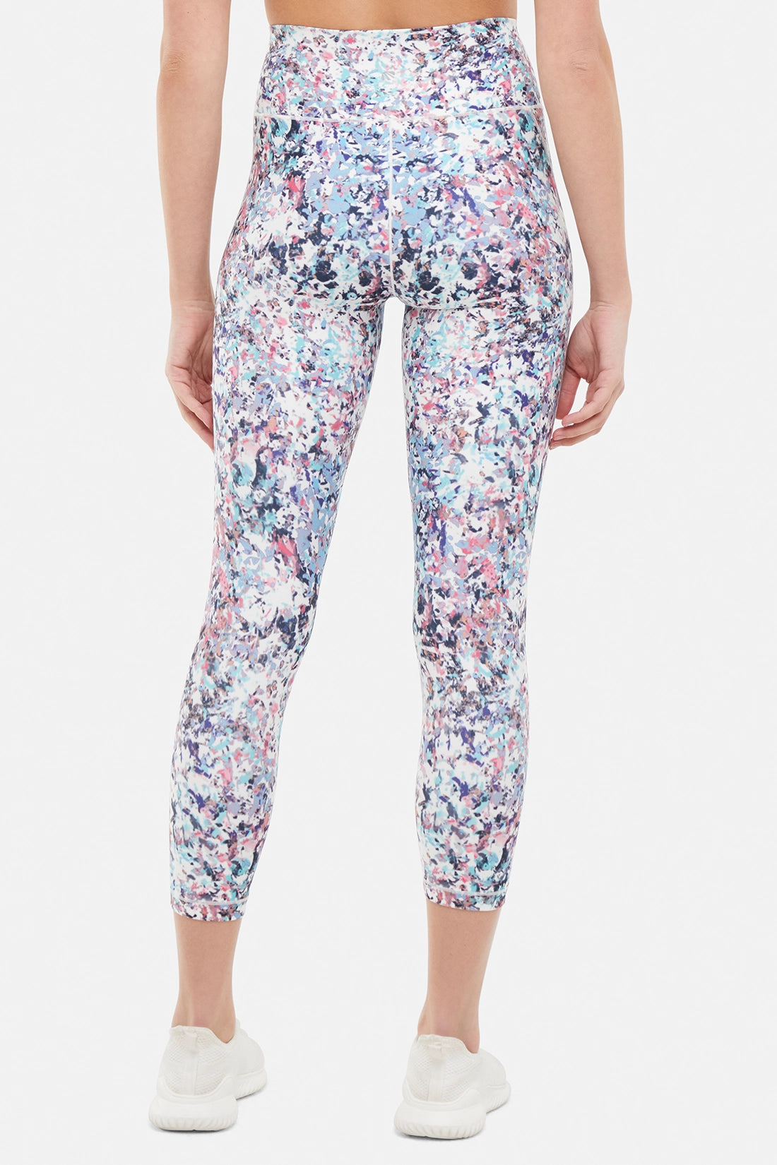 Back view of woman wearing colorful floral capris on a white background.