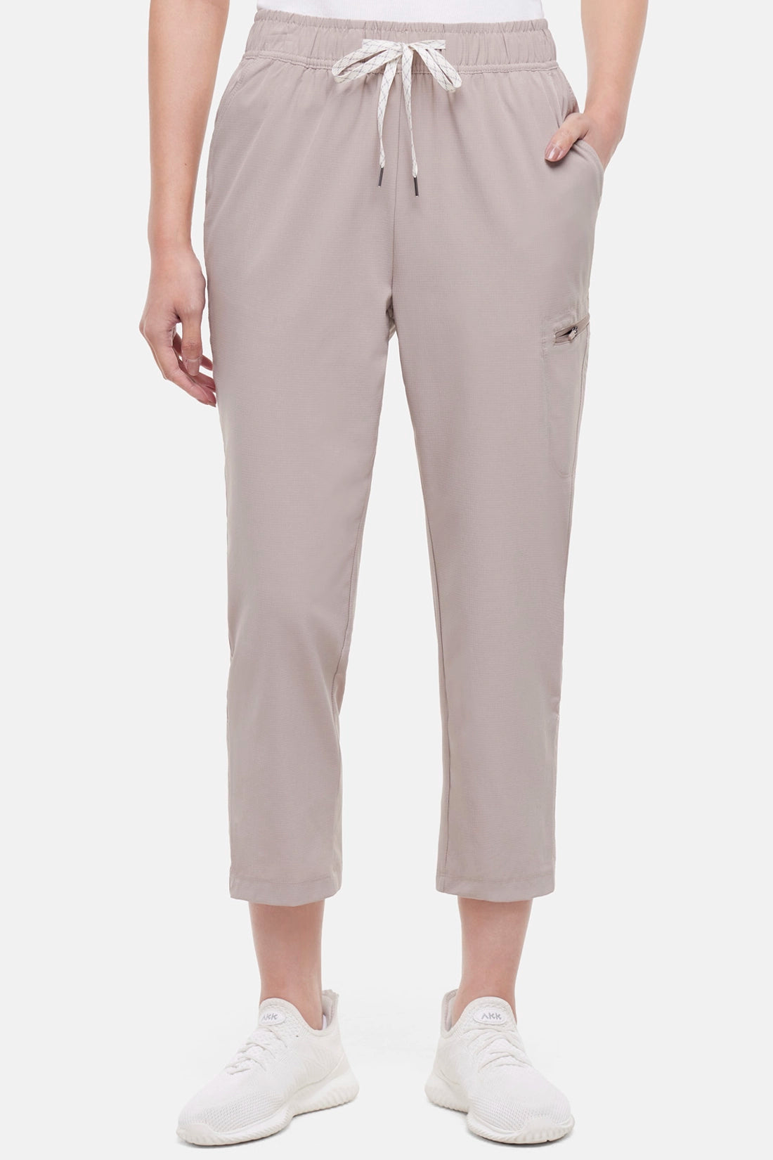 Front view of beige pants worn by a woman with hand in pocket white drawstring waist on a white background.