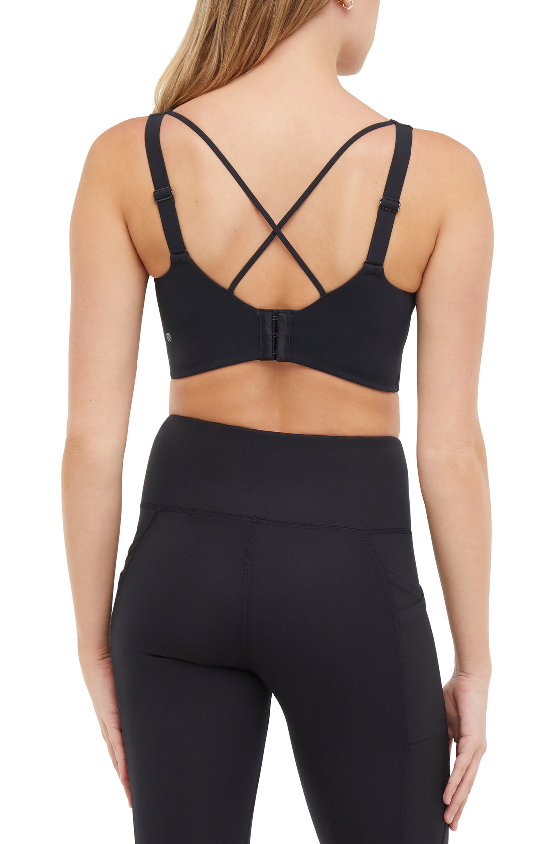 Back view of woman wearing a black sports bra and matching black leggings on a white background.