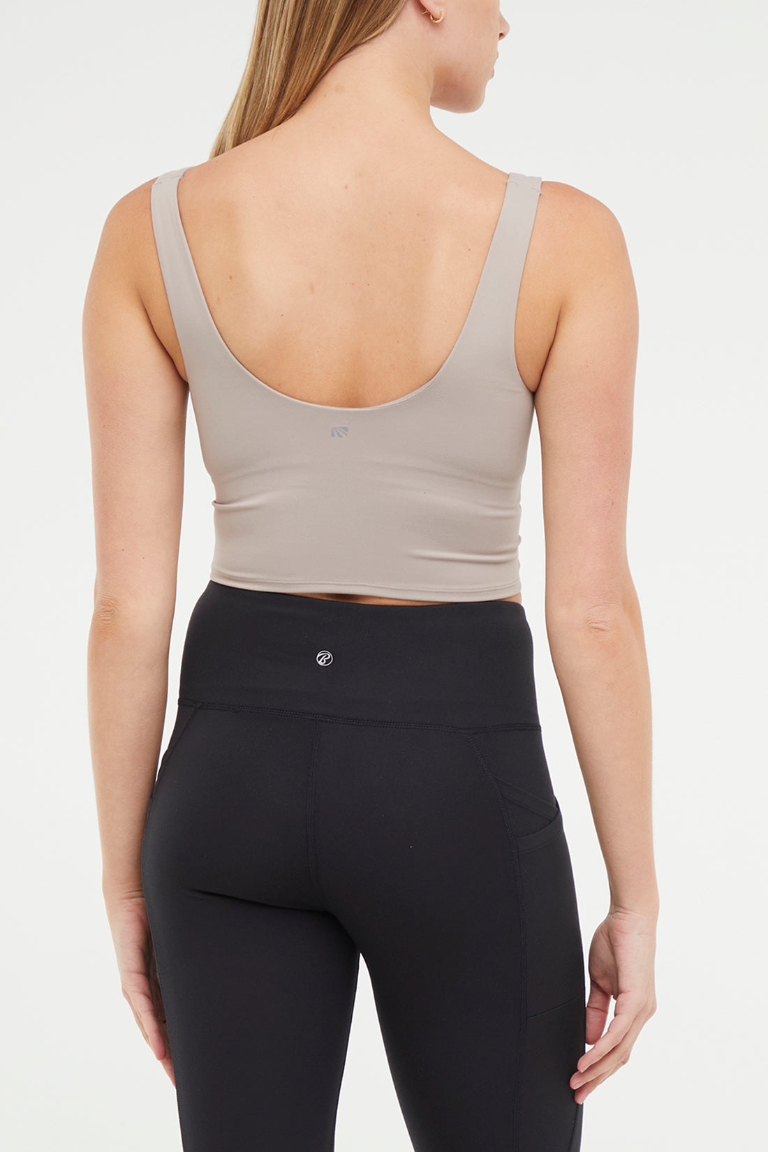 Close up back view of woman wearing a beige sports bra and black leggings on a white background.