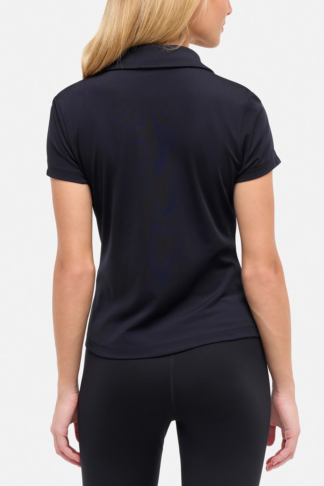 Back view of woman wearing a black polo shirt and black pants on a white background.