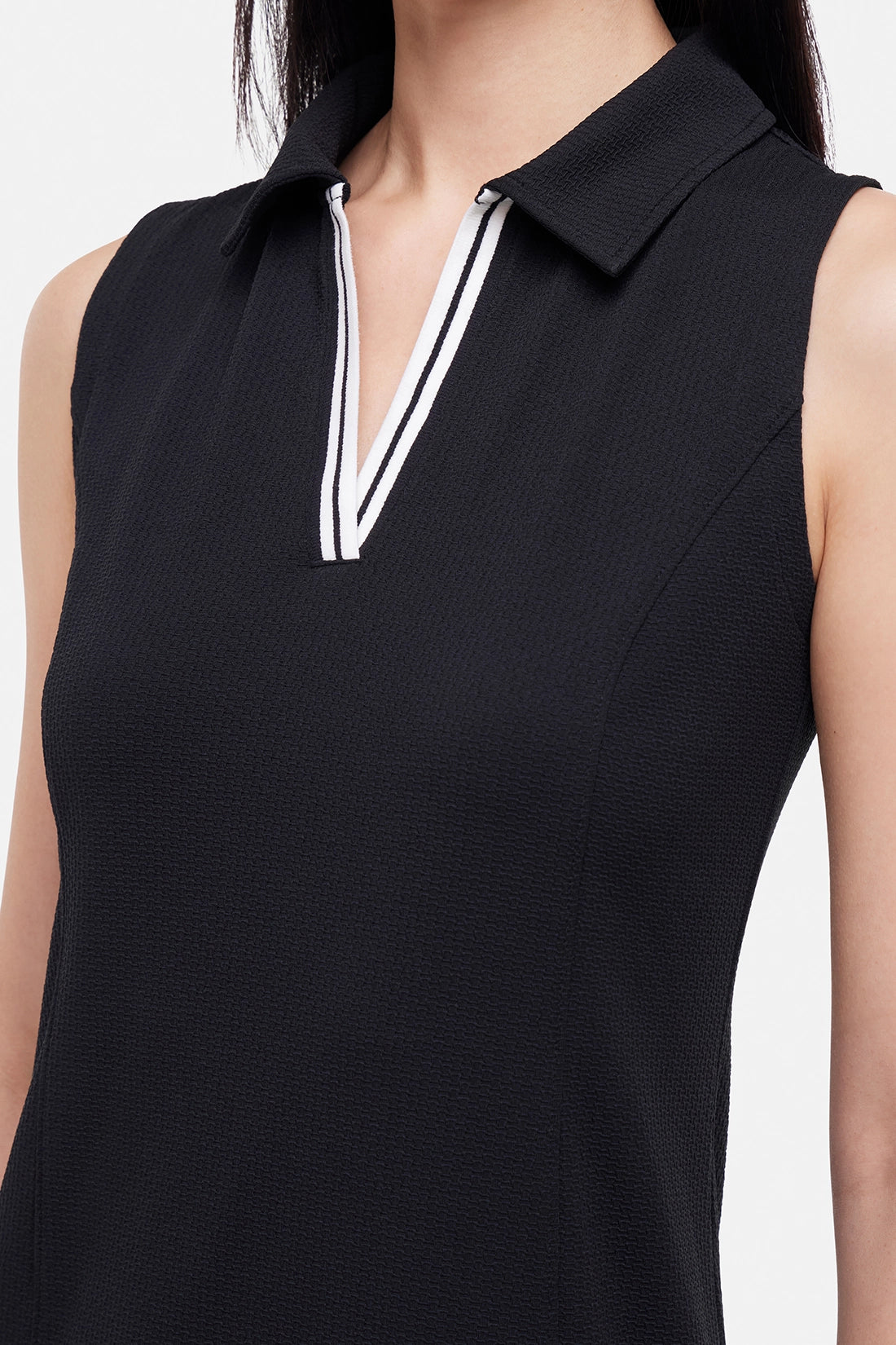 Close up front view of woman wearing a black sleeveless polo dress with a white stripe collar on a white background.
