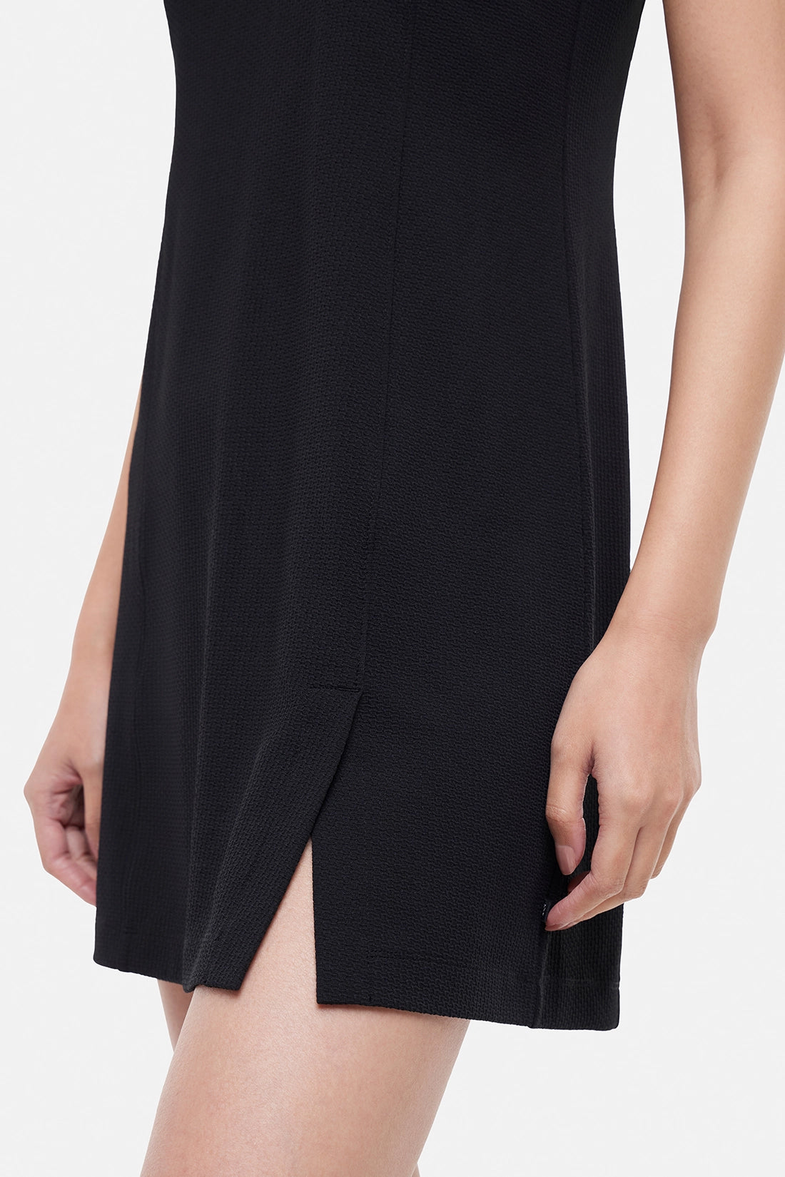 Front close up view of woman wearing a black sleeveless polo dress with slit on bottom hem on a white background.