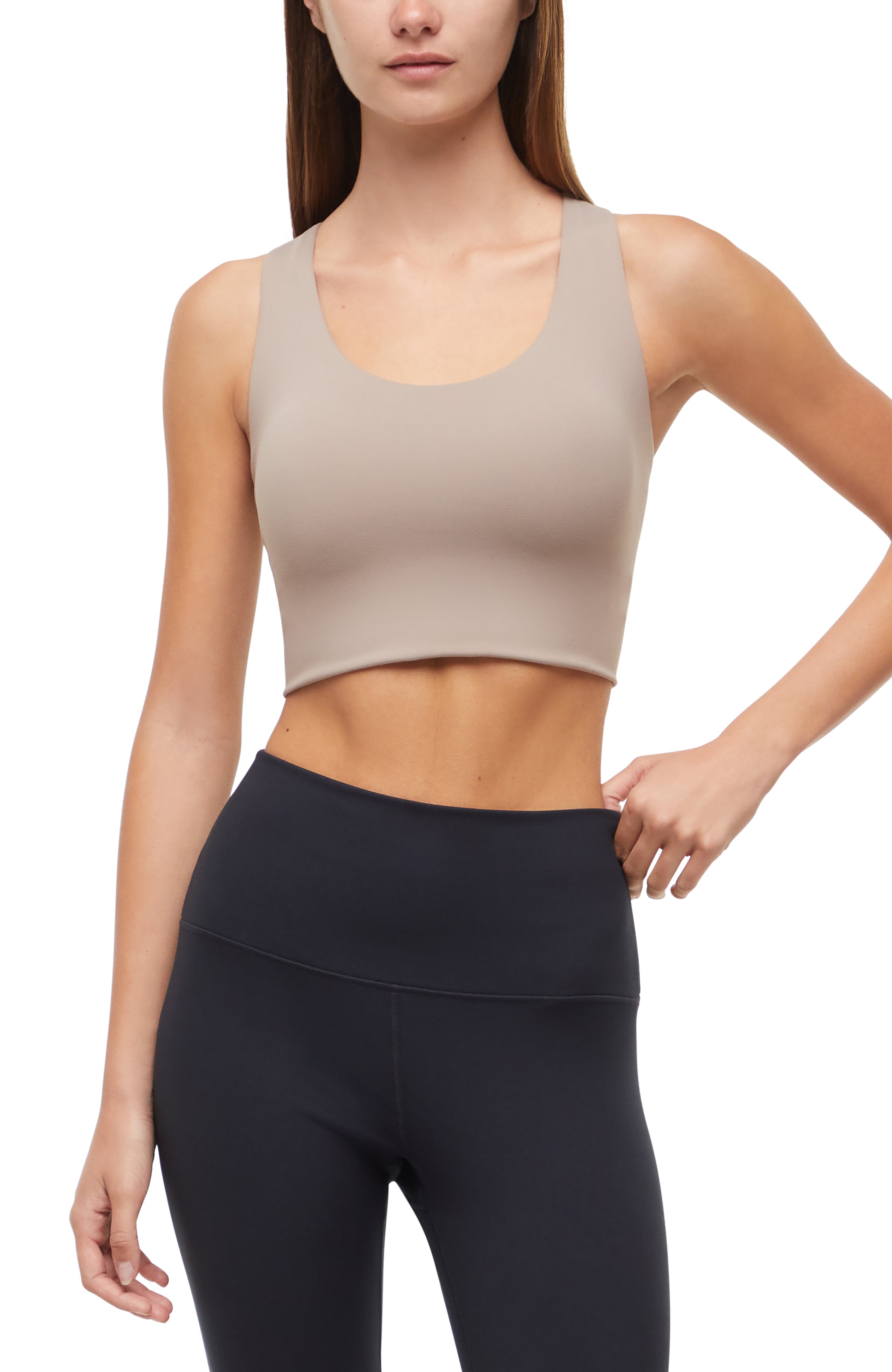 Front view of woman wearing a beige sports bra and black leggings on a white background.