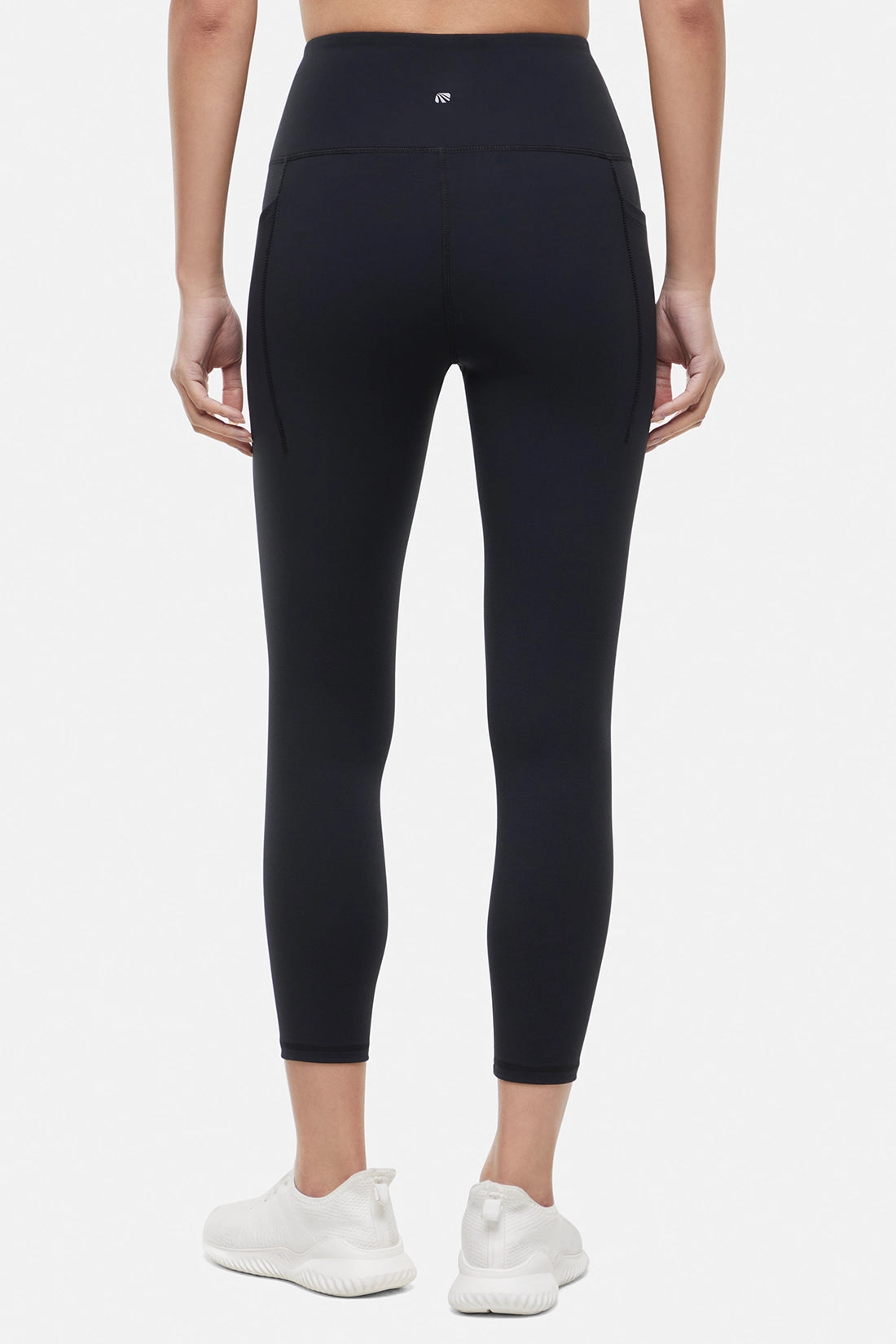 Back view of woman wearing black leggings worn by a person on a white background.