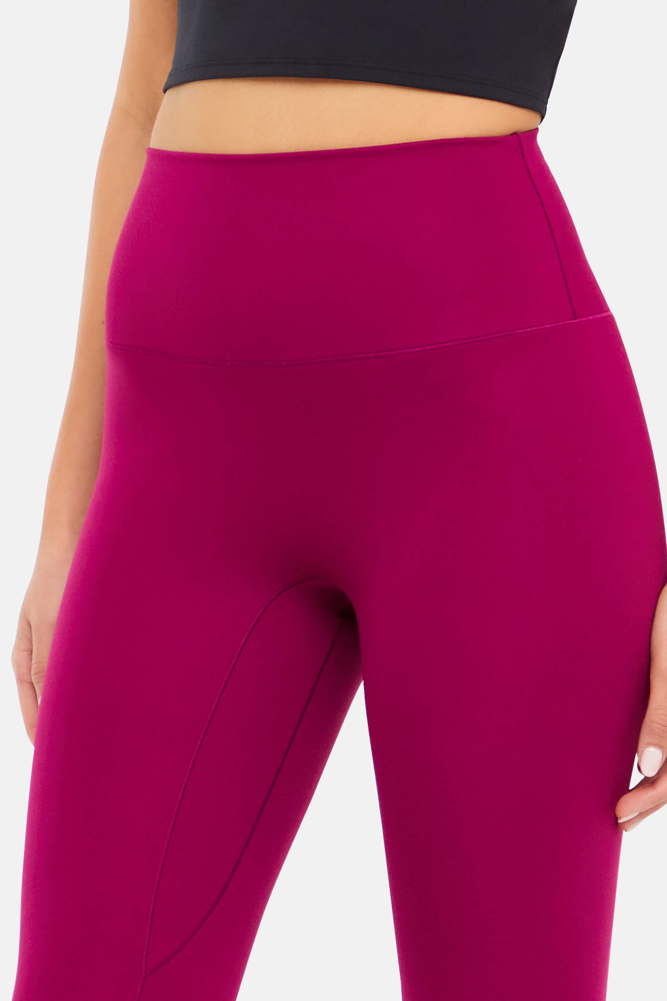 Close-up front view of woman wearing bright burgundy leggings on a white background.