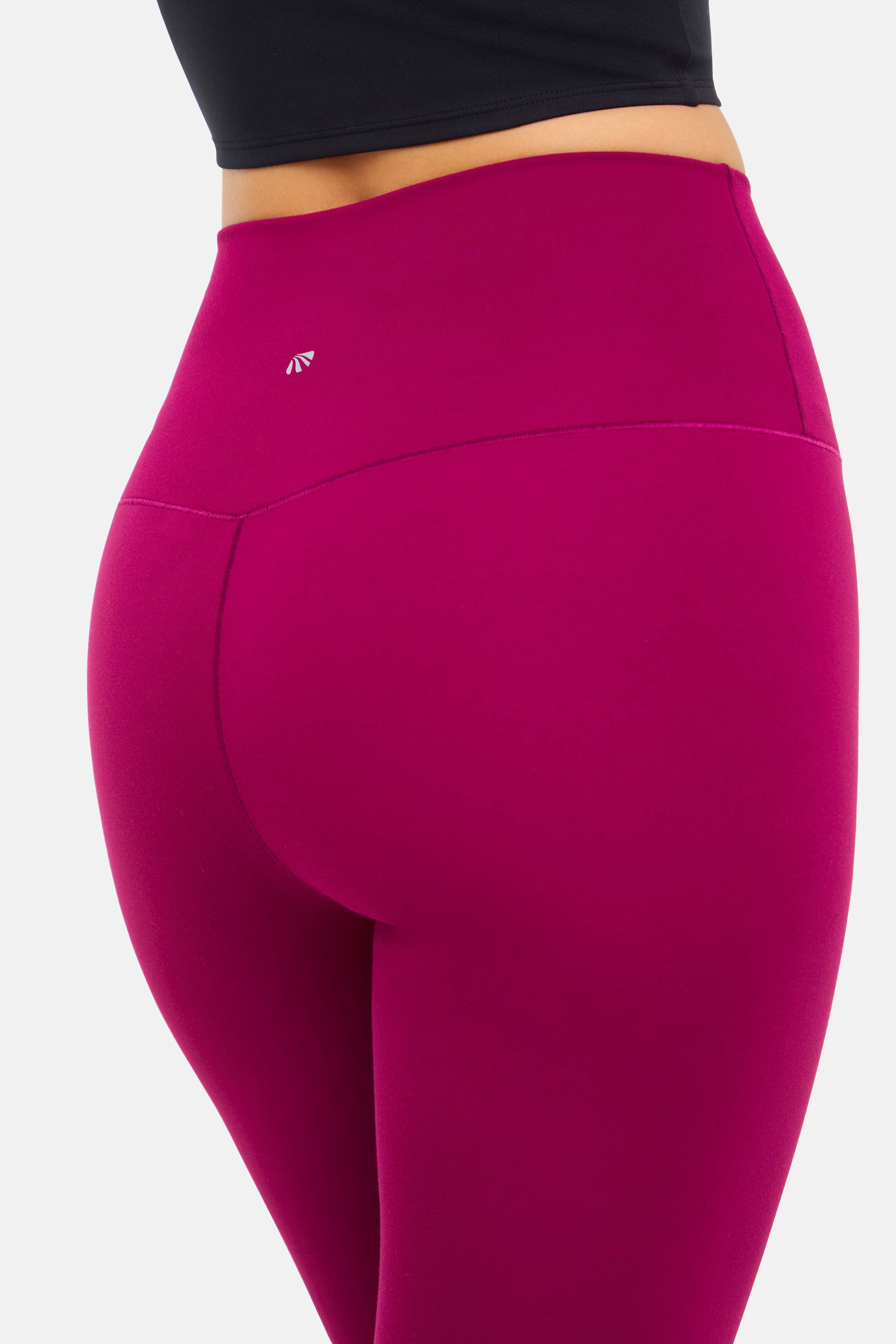 Close up back view of woman wearing bright burgundy leggings with small white logo on a white background.