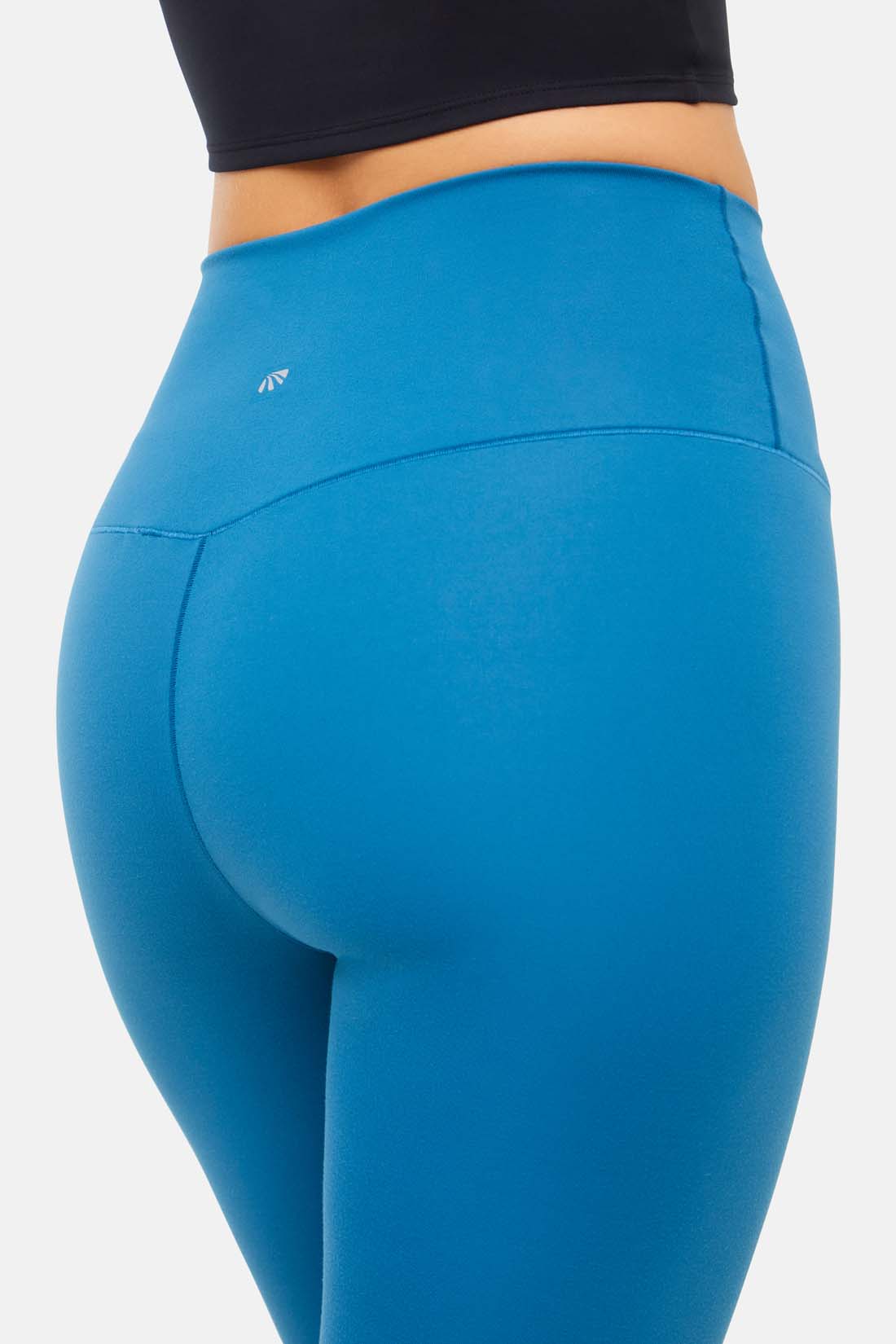 Close up back view of woman wearing bright blue leggings on a white background.