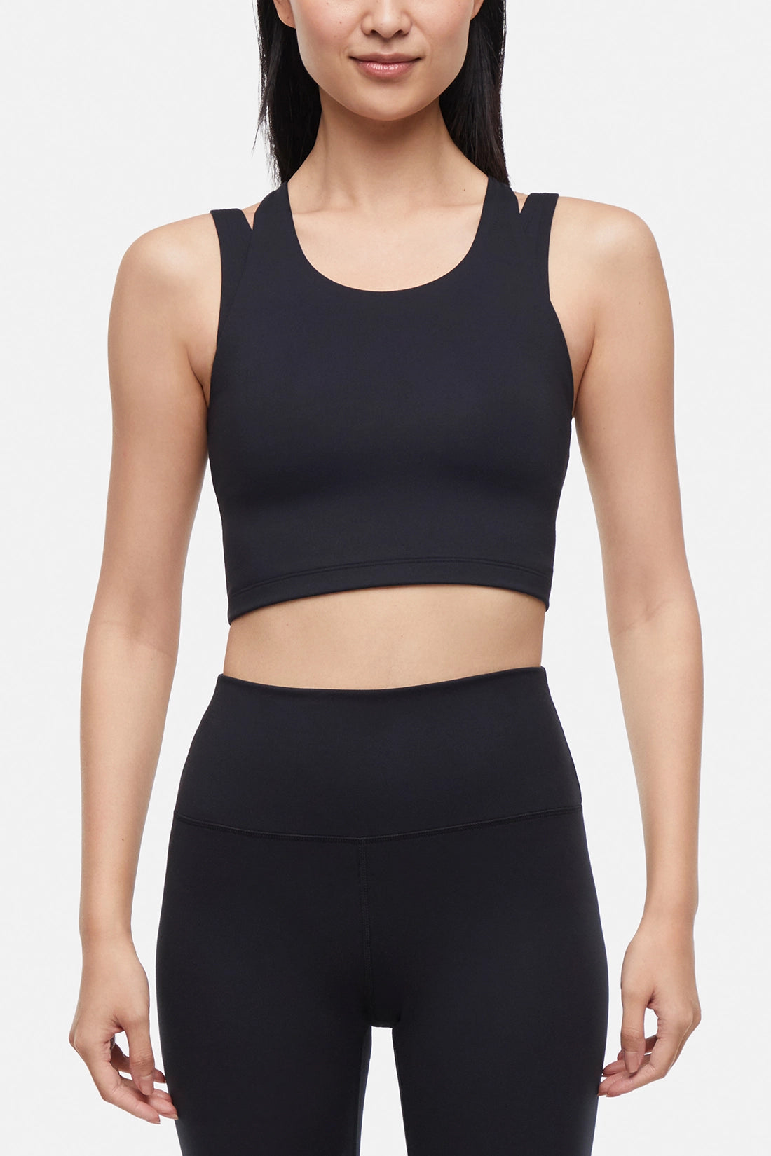 Front view of woman wearing a black sports bra and black leggings on a white background.