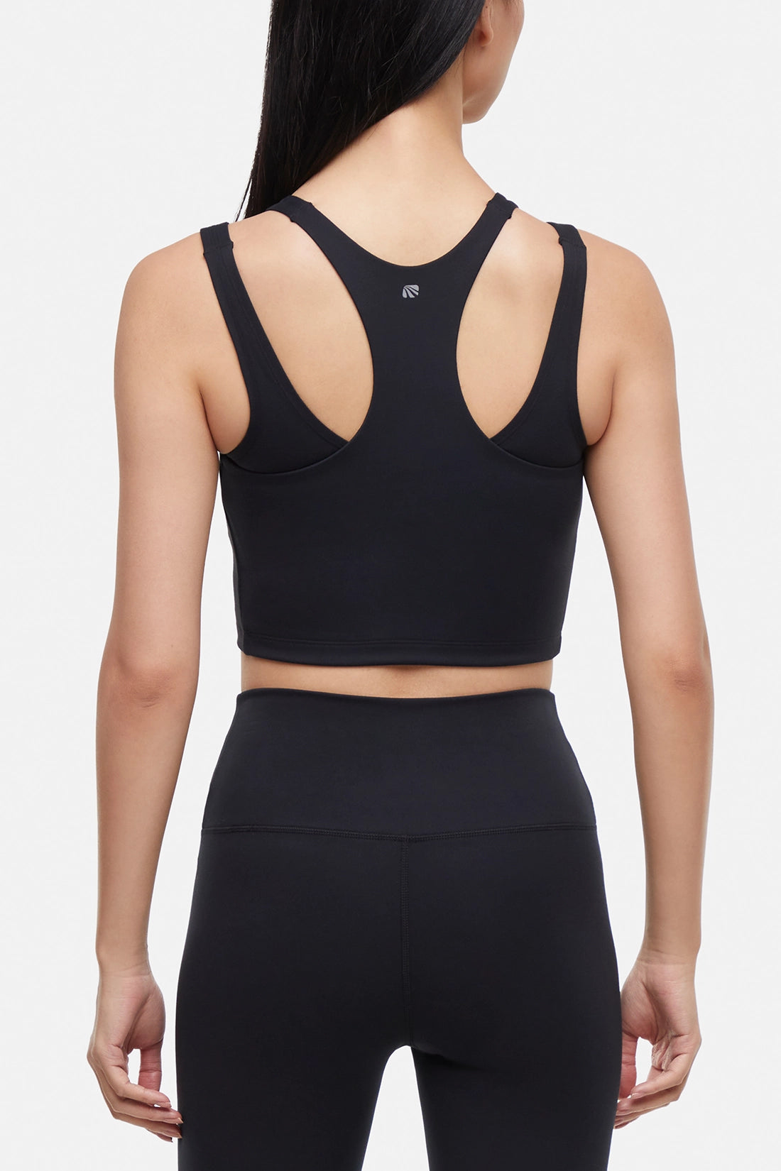 Back view of woman wearing a black sports bra and black leggings on a white background.