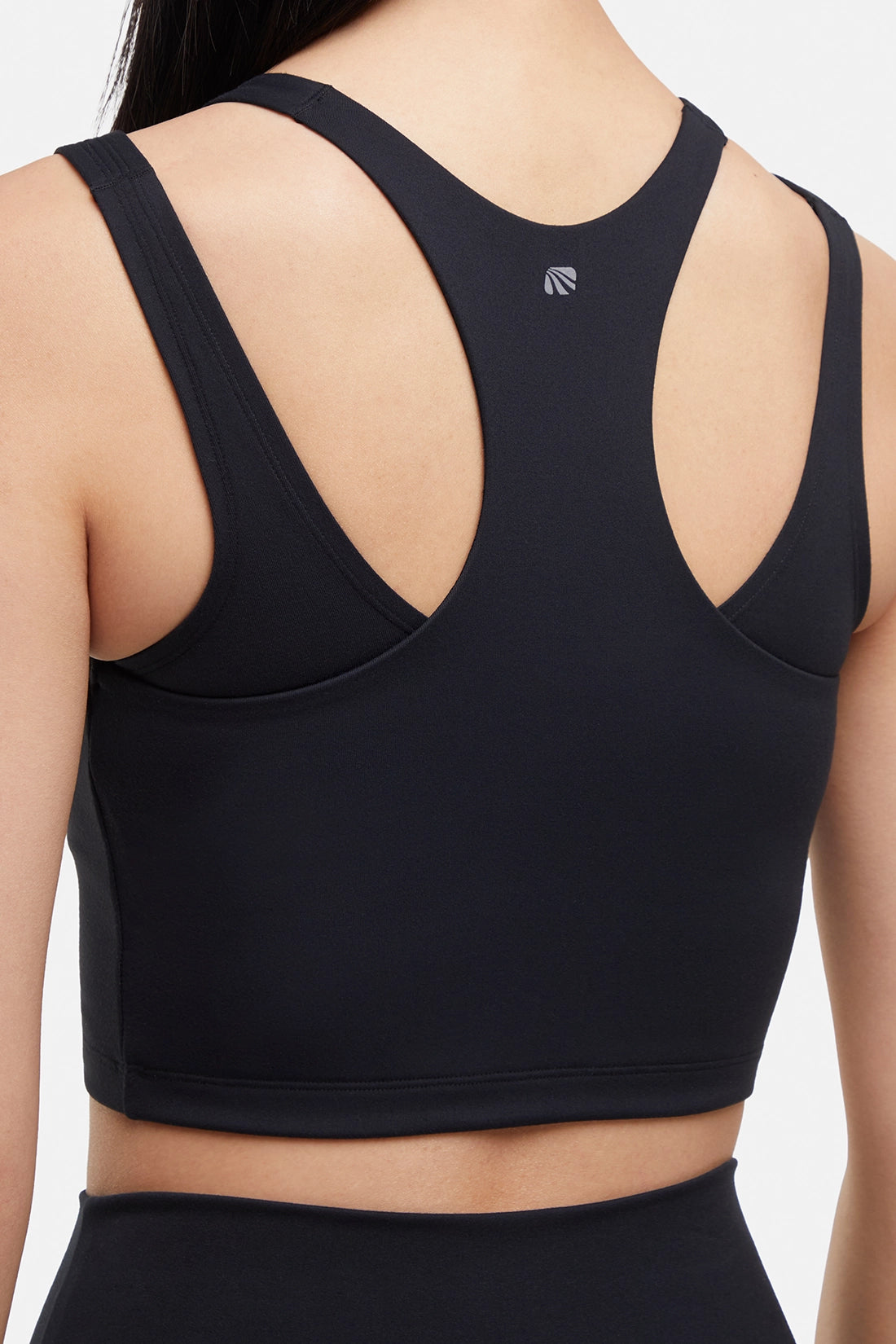 Close up back view of woman wearing a black sports bra and black leggings on a white background.