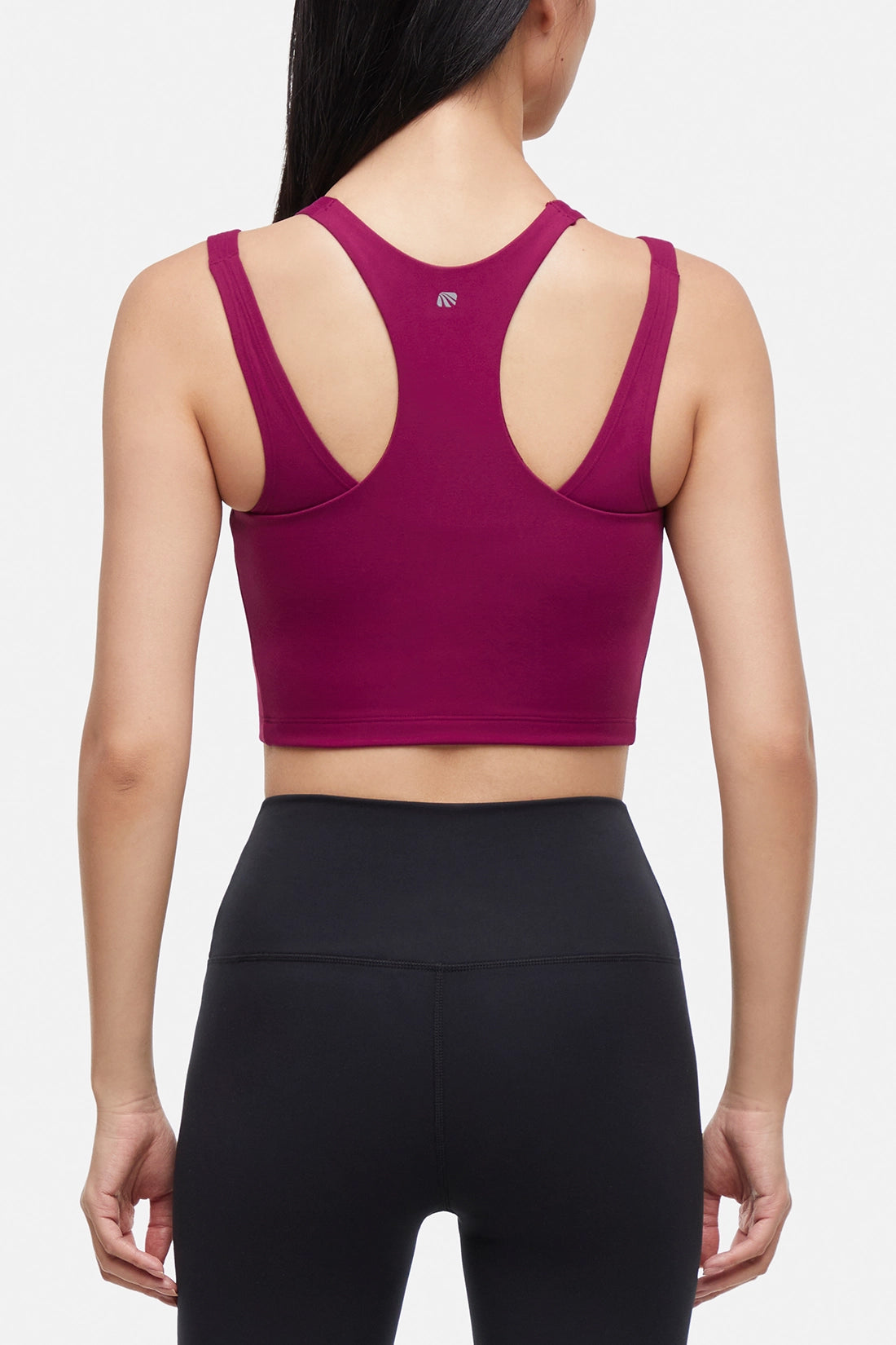 Back view of woman wearing a bright burgundy sports bra and black leggings on a white background.