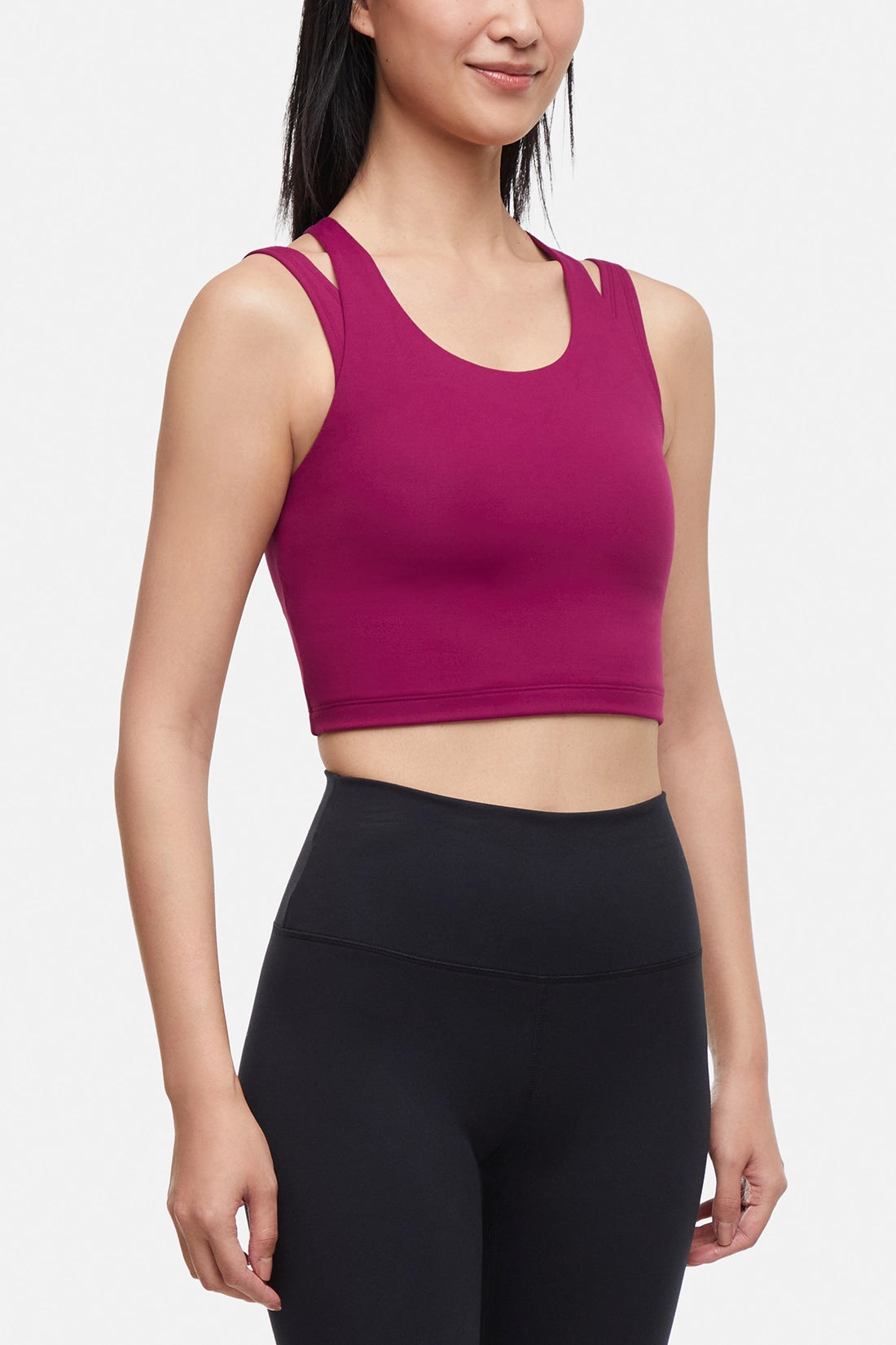 Side view of woman wearing a bright burgundy sports bra and black leggings on a white background.