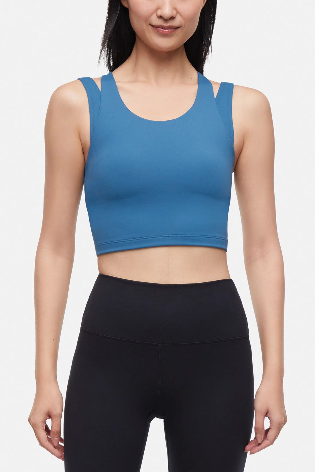 Front view of woman wearing a blue sports bra and black leggings on a white background.