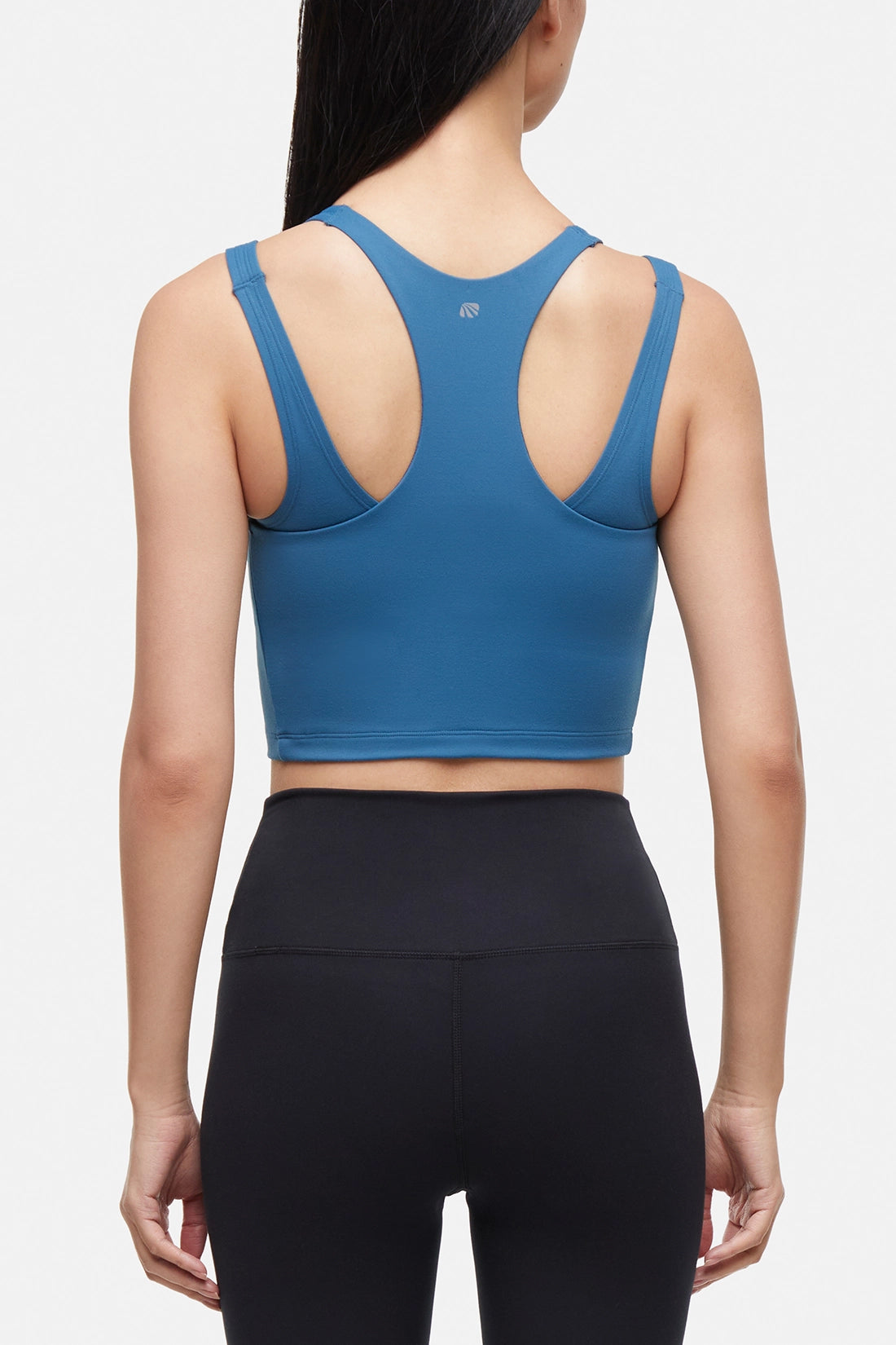 Back view of woman wearing a blue sports bra and black leggings on a white background.
