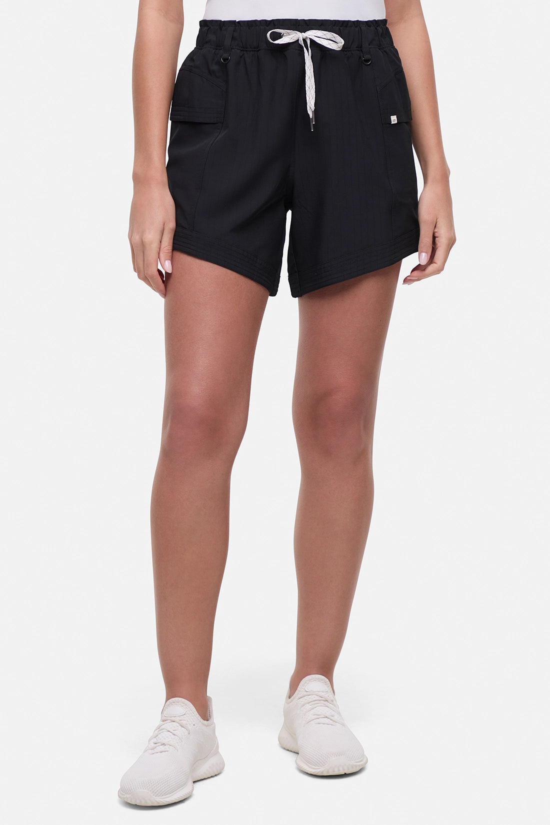 Front view of woman wearing black shorts with white drawstring waist and white sneakers on a white background.