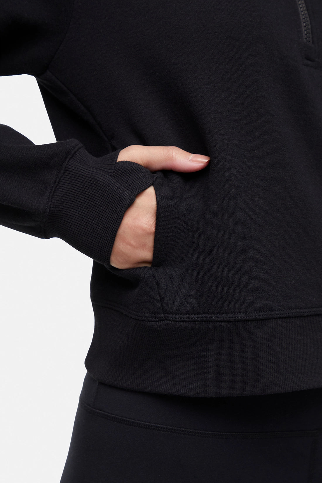 Front close up view of woman wearing black half-zip pullover with thumbholes on a white background.