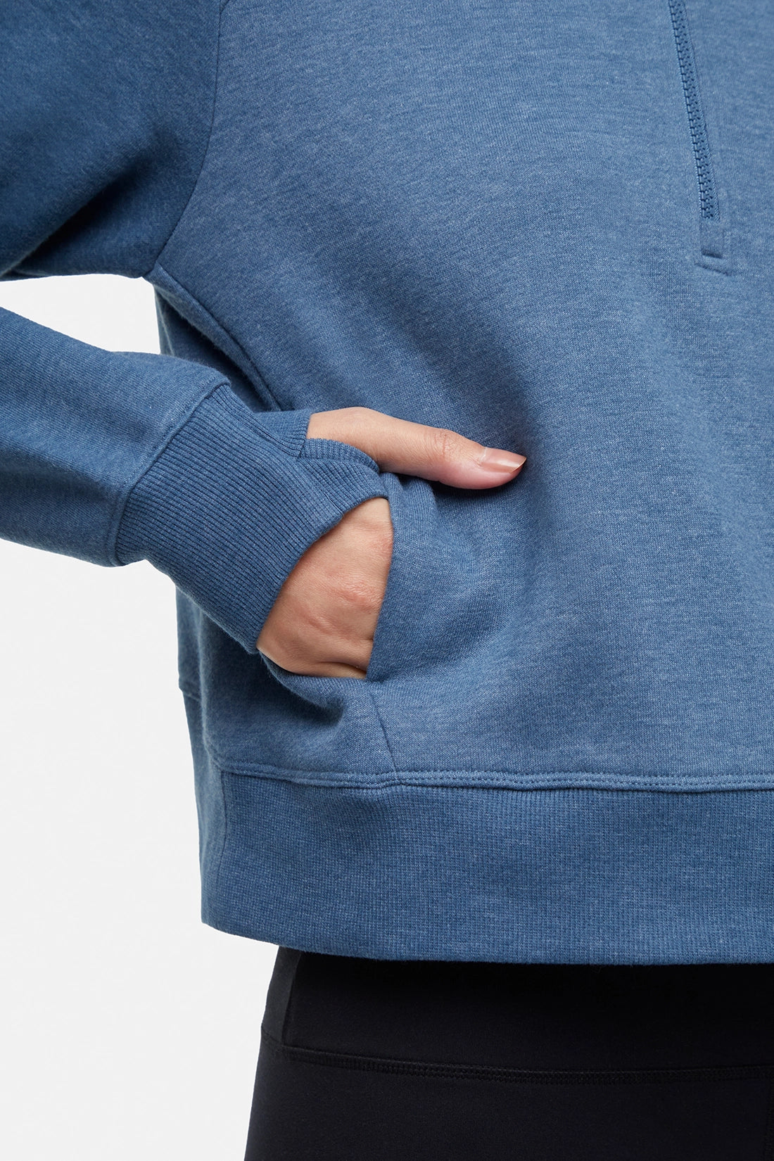 Close up view of woman wearing heather blue half-zip pullover with thumbholes on a white background.