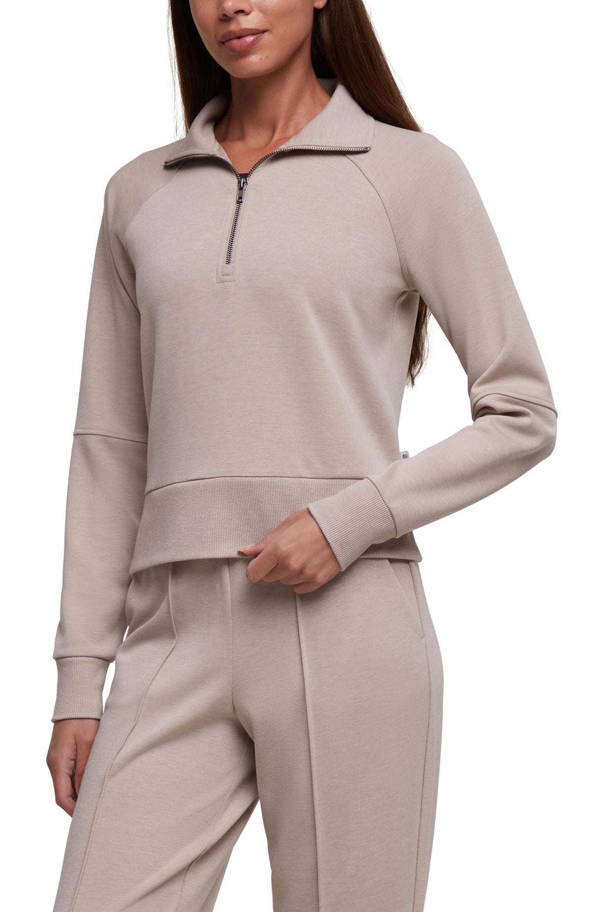 A woman wearing a light taupe-beige long-sleeve quarter-zip pullover and matching jogger pants against a plain white background.