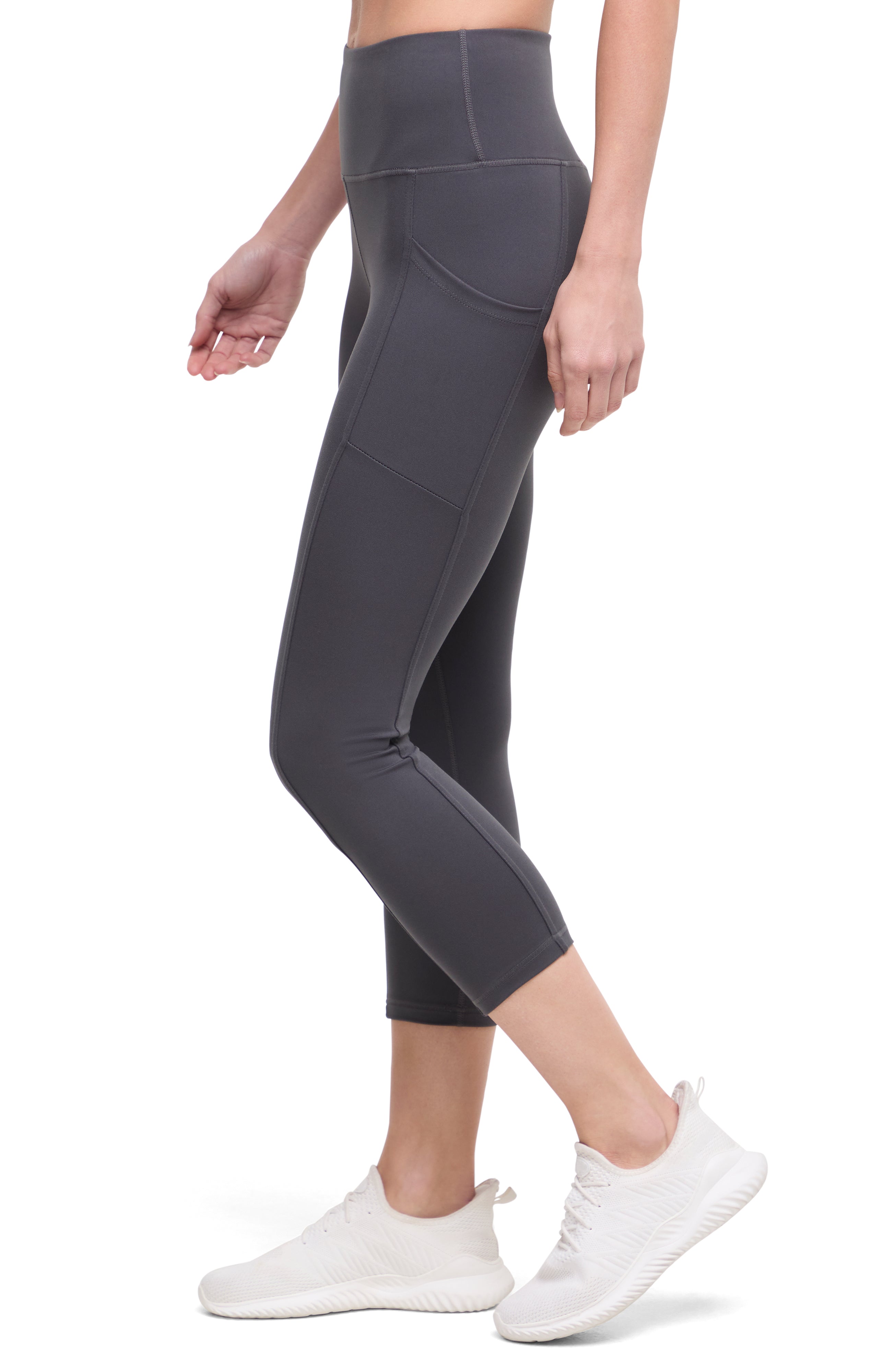 Side of woman wearing dark gray leggings with a white background.