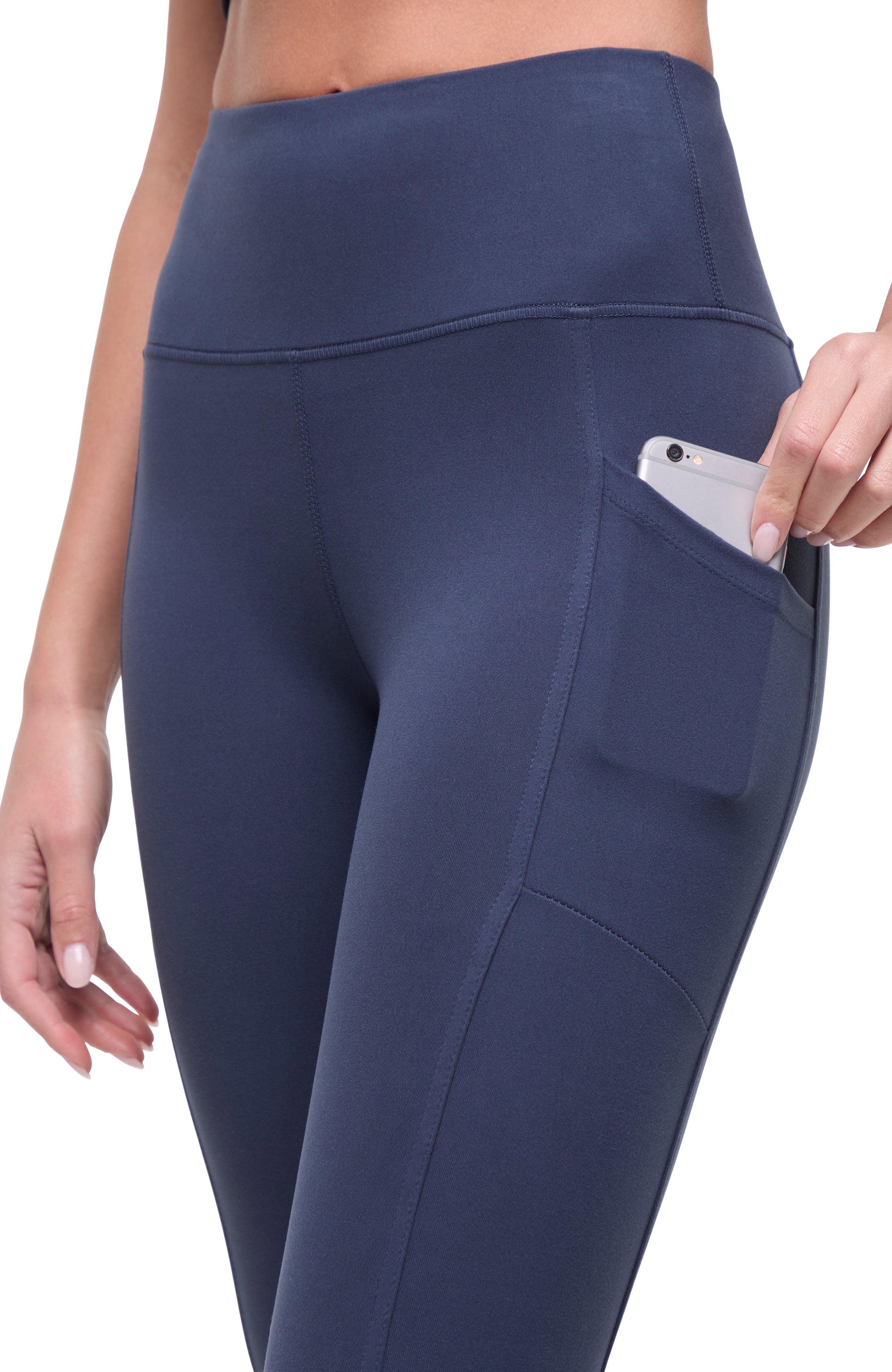 Side view of woman wearing navy blue leggings with hand in pocket on a white background.