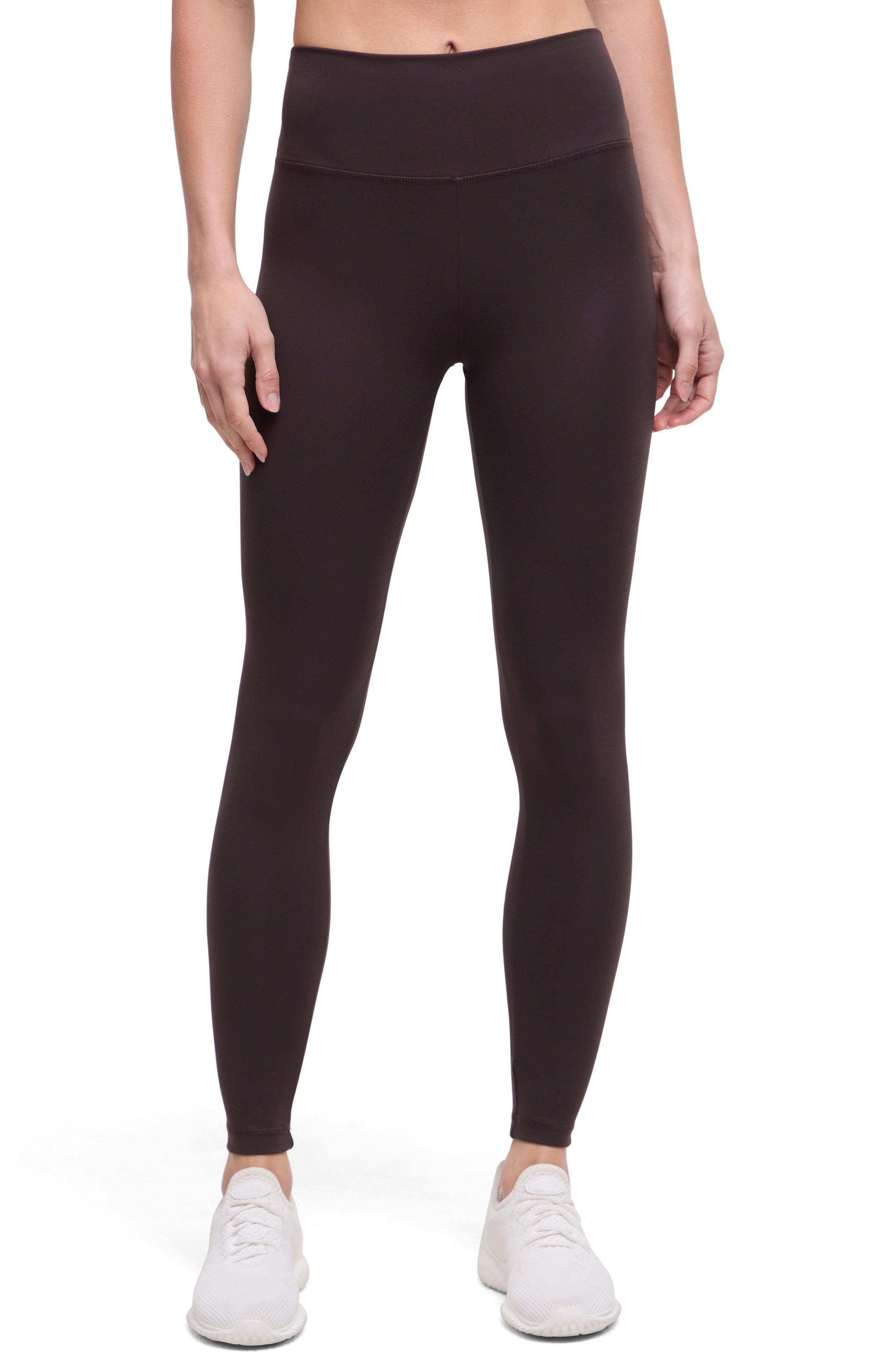 Front view of woman wearing dark brown leggings with a white background.