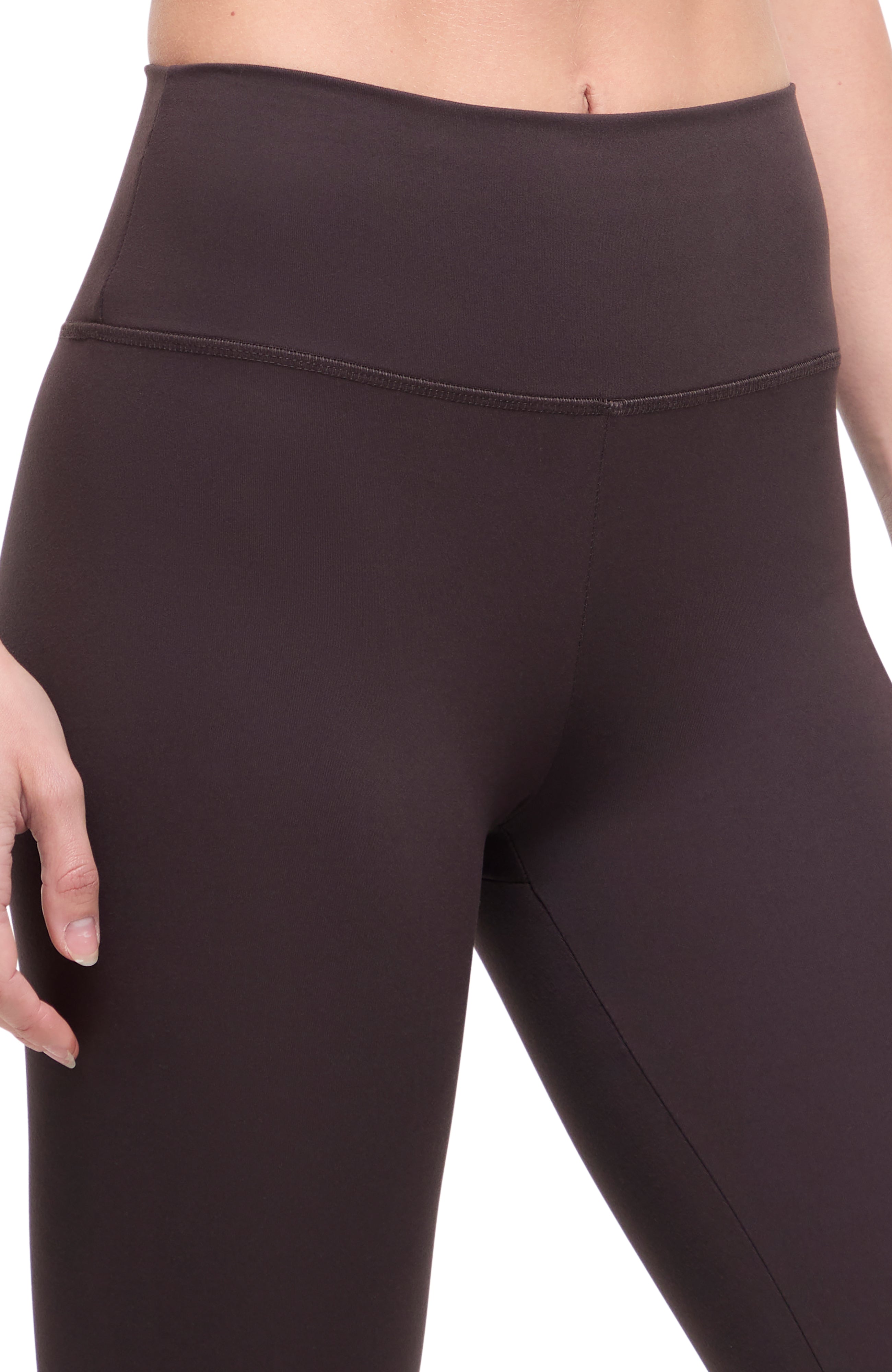 Close up front view of woman wearing dark brown leggings with a white background.