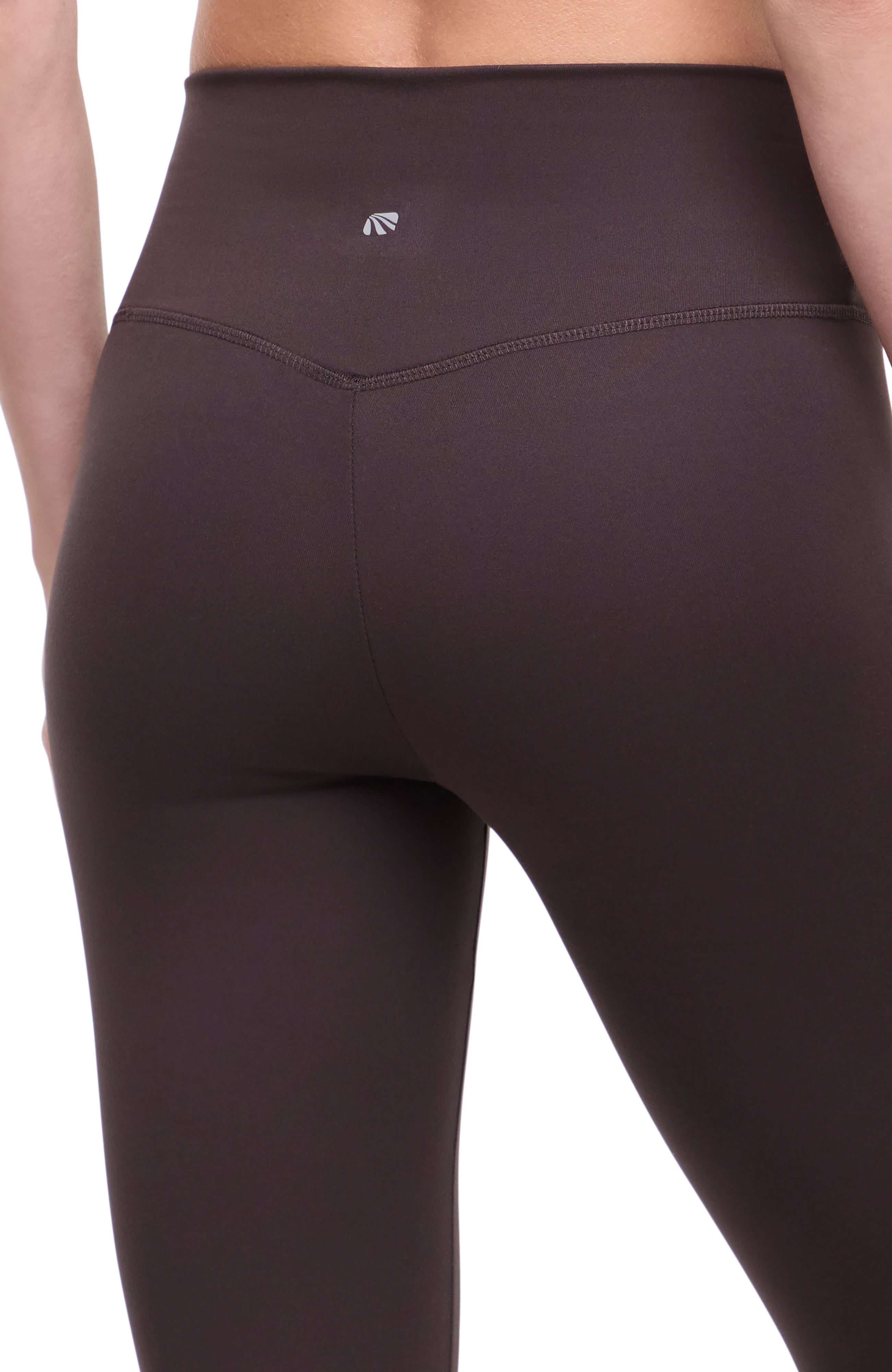 Close up back view of woman wearing dark brown leggings with a white background.