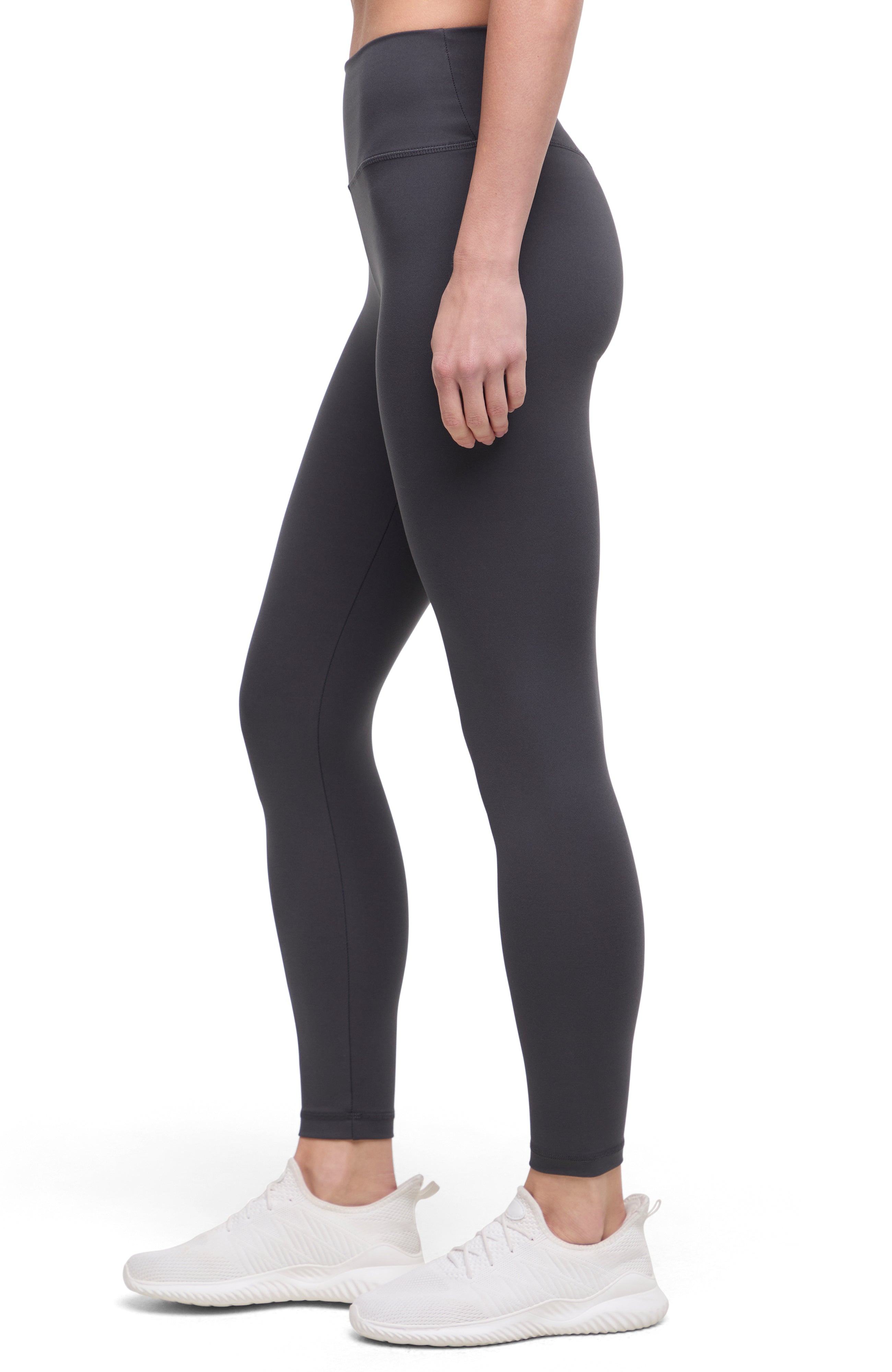 Side view of woman wearing dark gray leggings with a white background.