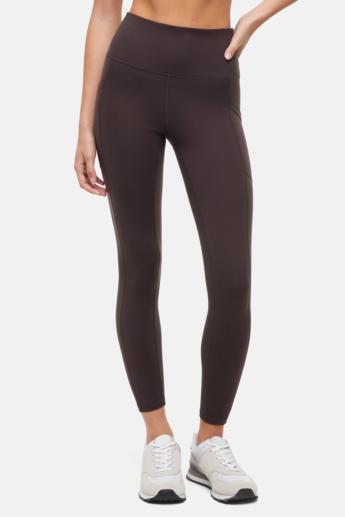Front view of woman wearing dark brown leggings with a white background. 