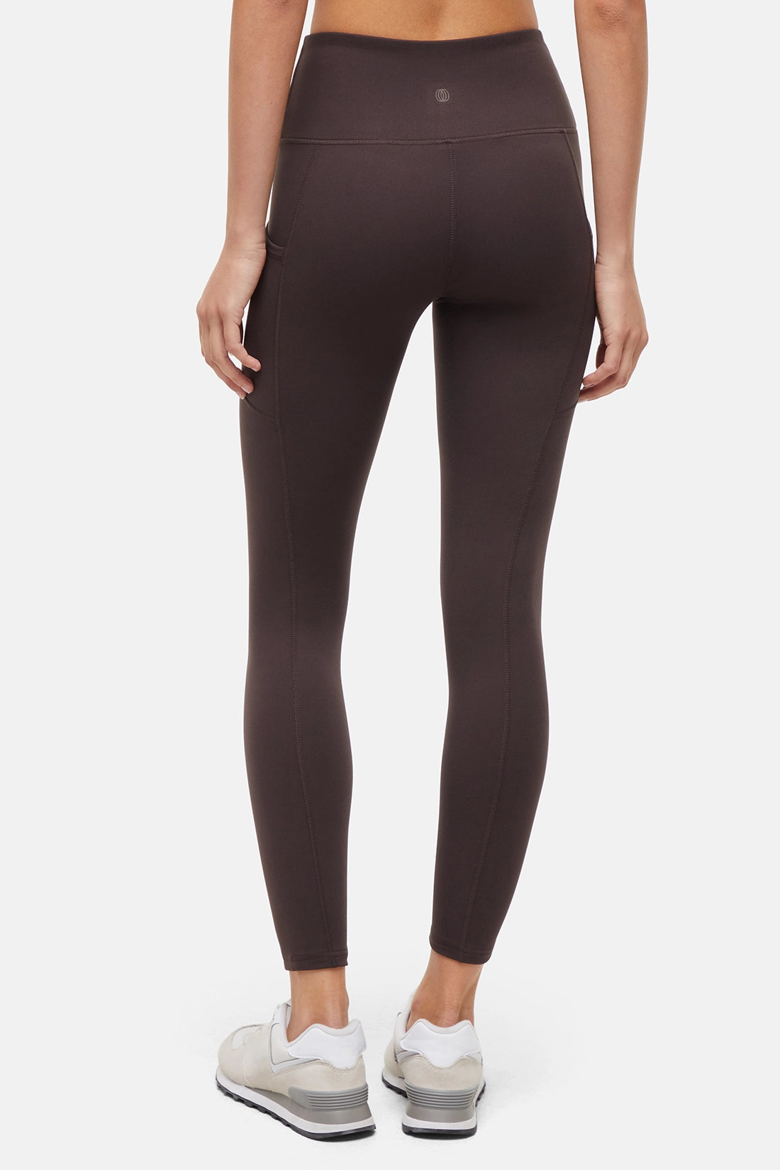 Back view of woman wearing dark brown leggings with a white background. 