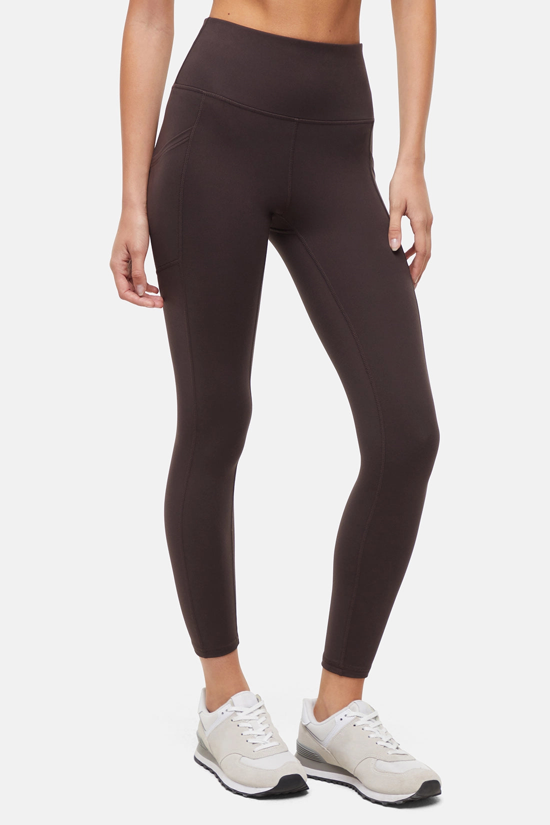 Front view of woman wearing dark brown leggings with a white background. 