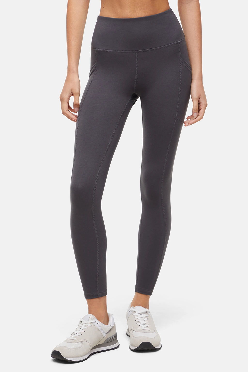 Front view of woman wearing dark gray leggings with a white background. #color_forged-iron