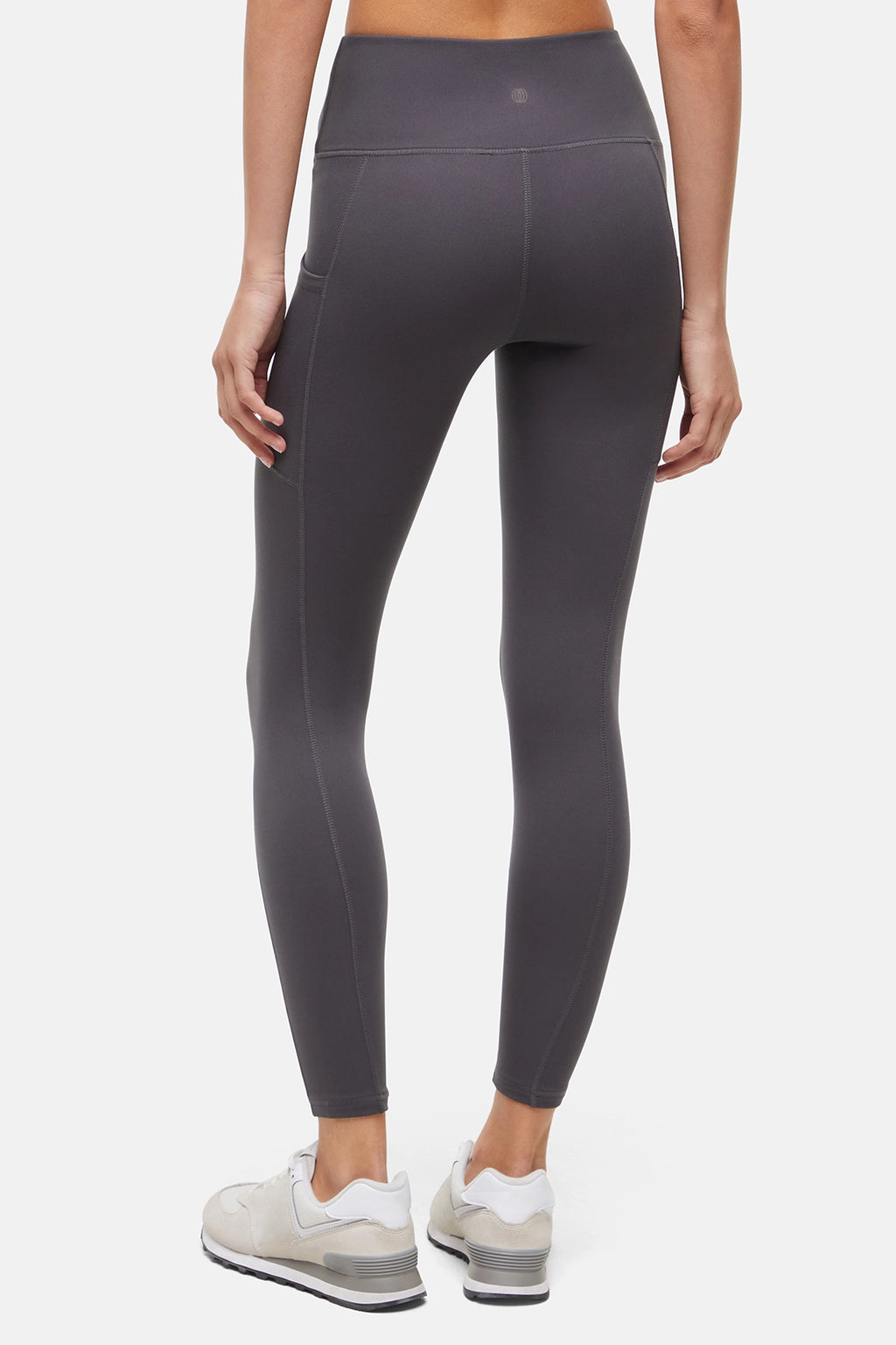 Back view of woman wearing dark gray leggings with a white background. #color_forged-iron