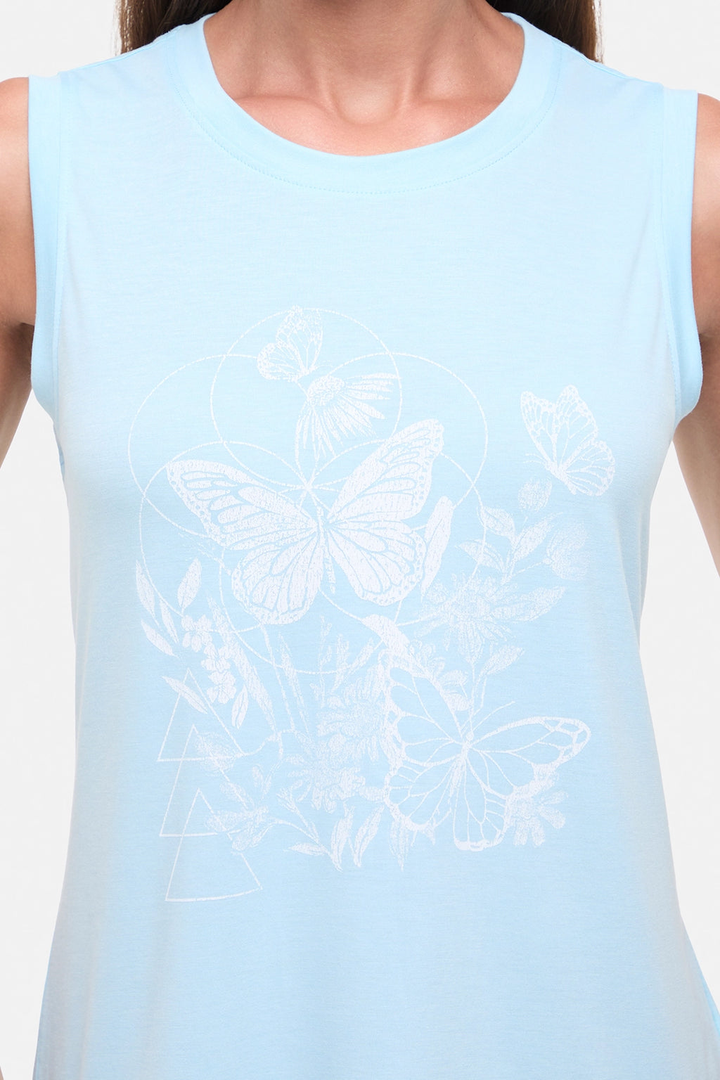 Close up view of woman wearing a light blue sleeveless top with white butterflies design on a plain background. #color_heather-ocean-current-butterfly-bunch