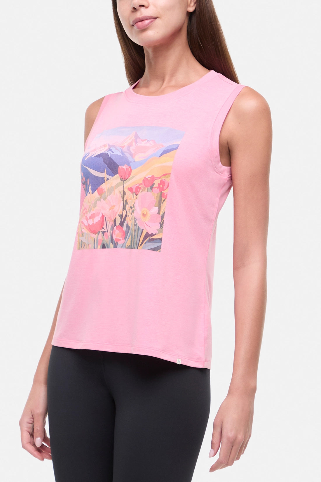Side view of woman wearing a pink sleeveless top with a colorful floral and mountain design on a white background.