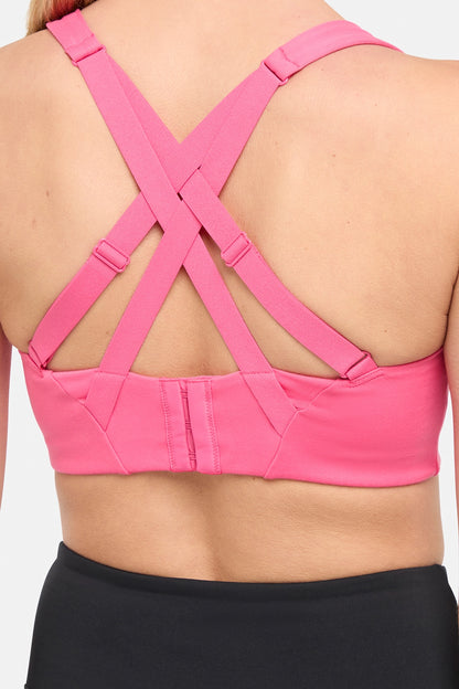 Close up back view of pink sports bra with strappy crisscross straps on a plain background. 