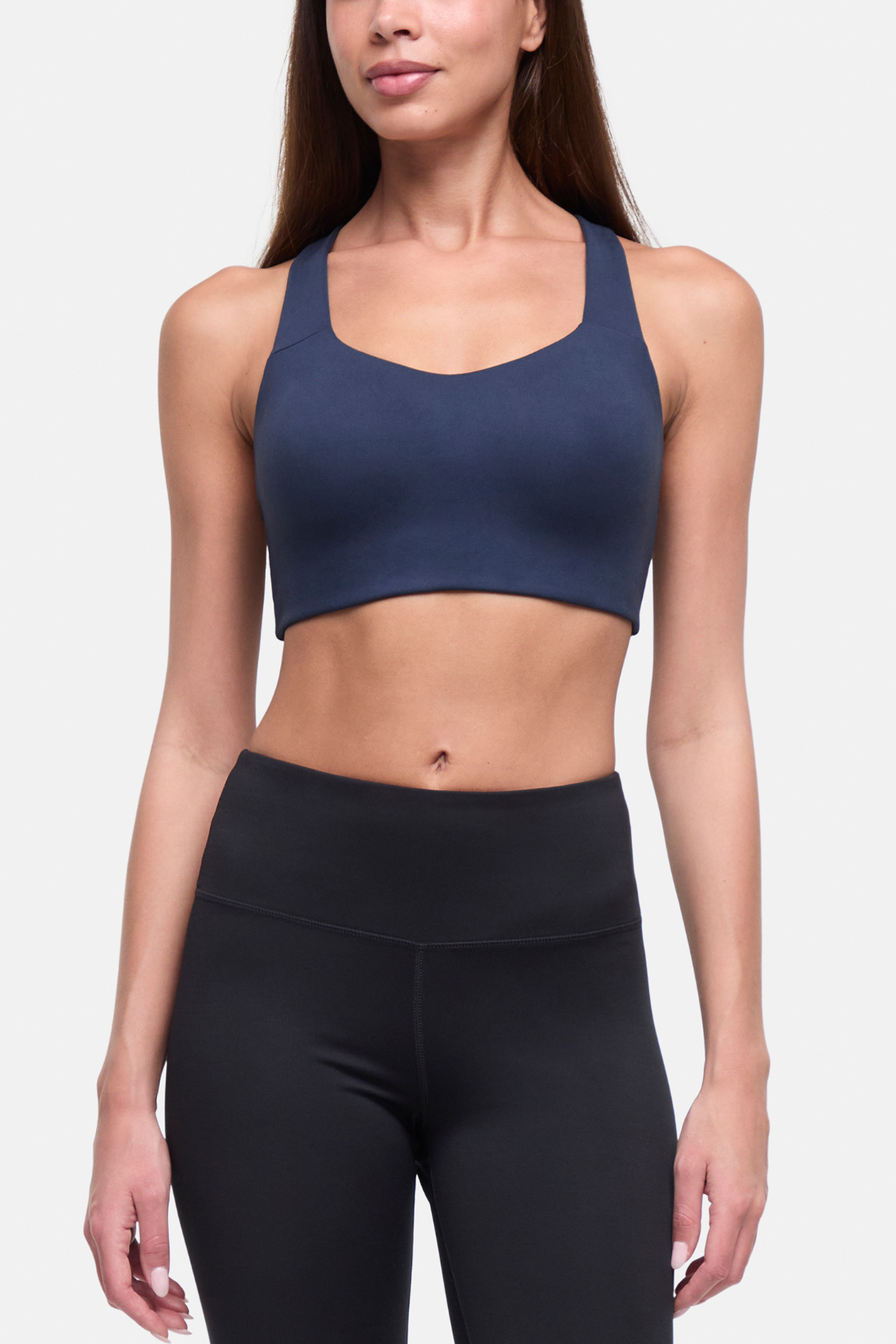 A woman modeling a navy blue sports bra and black high-waisted leggings against a light gray studio background. 