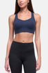 A woman modeling a navy blue sports bra and black high-waisted leggings against a light gray studio background. 